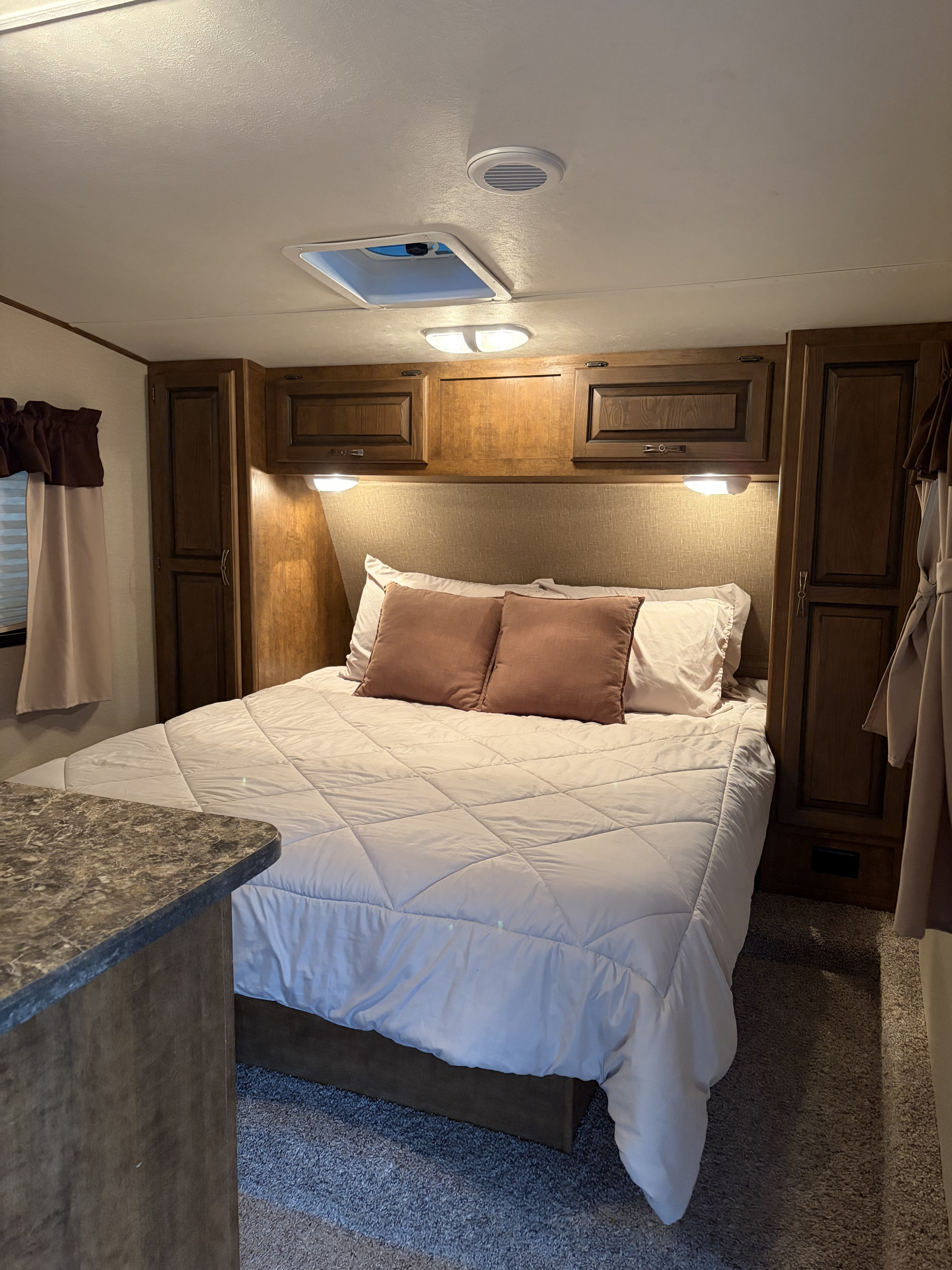 Cozy RV rental bedroom featuring a comfortable bed with soft lighting, overhead cabinets, and a vent, perfect for your travels.. Crossroads RV Rezerve 2016