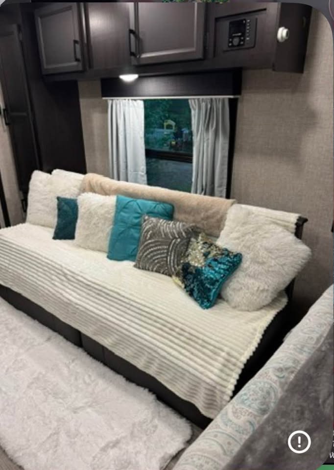 Comfortable RV rental interior with a cozy sofa/bed, accent pillows, overhead cabinets, and a window looking outdoors.. Jayco Jay Flight 2022