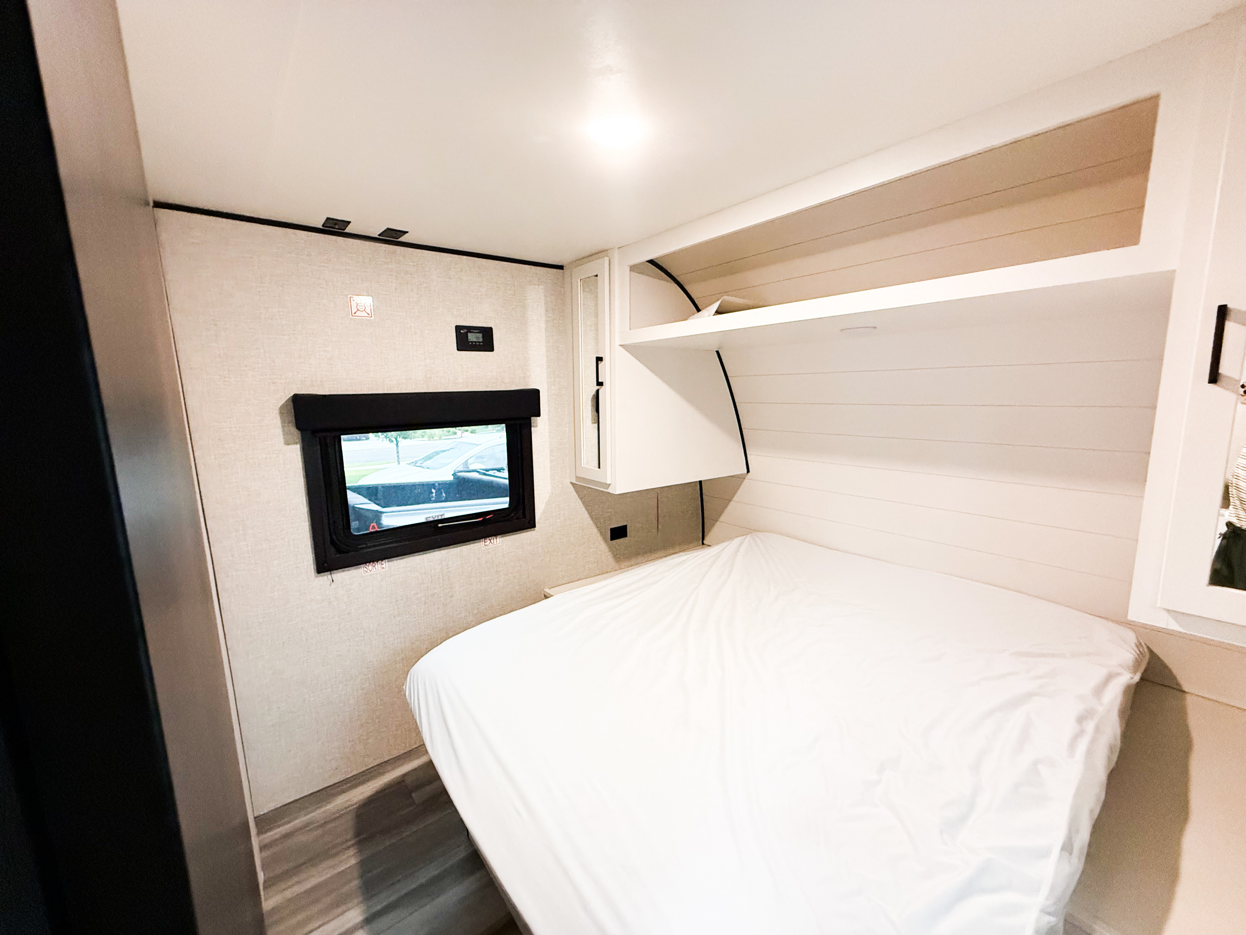 Modern RV rental bedroom interior: clean white bed, overhead storage, window with exterior view, and wall controls.. GOPLAY 26BH 2024