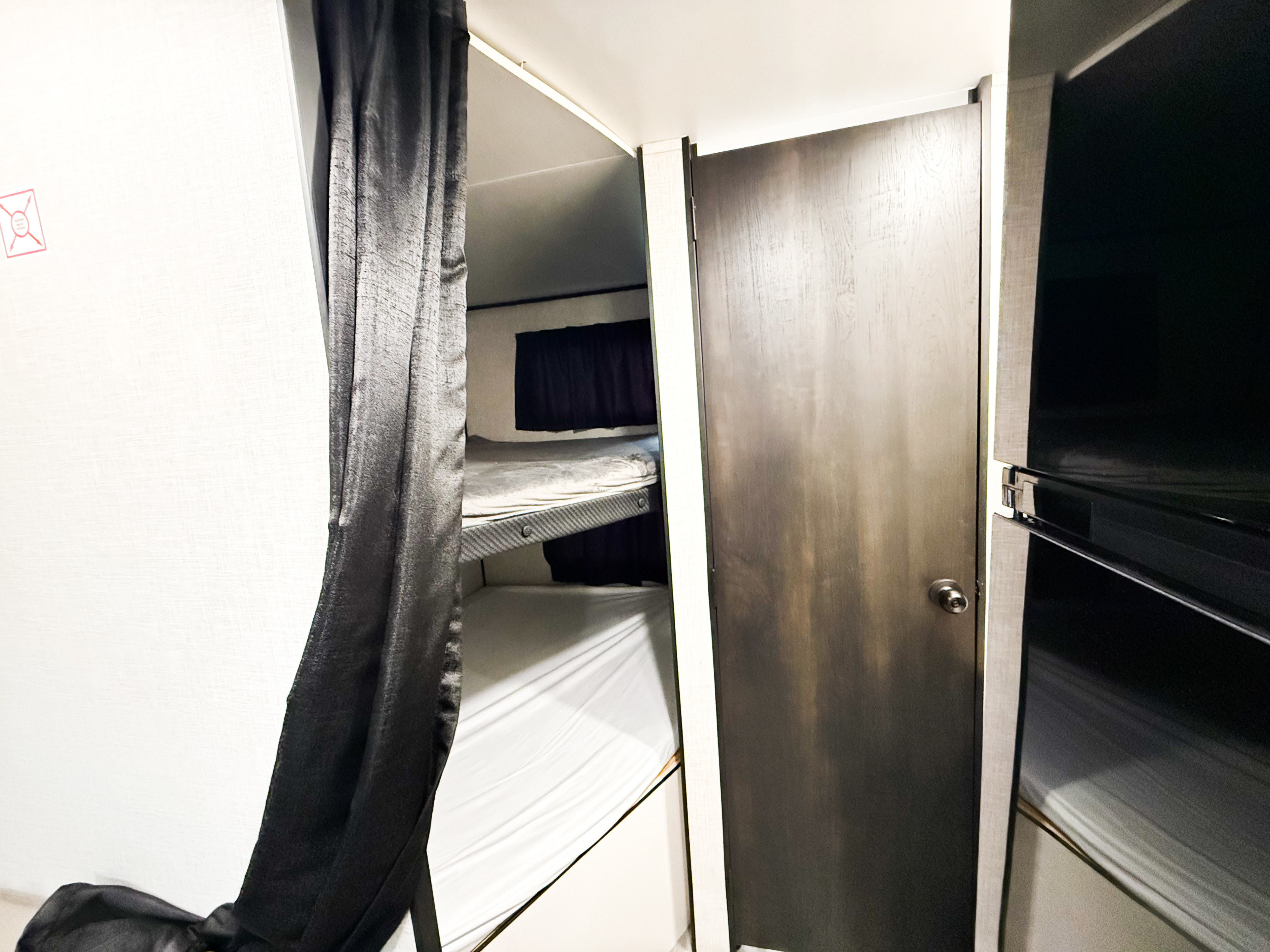 RV rental: Bunk beds with dark privacy curtains inside a compact interior, next to a closed door.. GOPLAY 26BH 2024