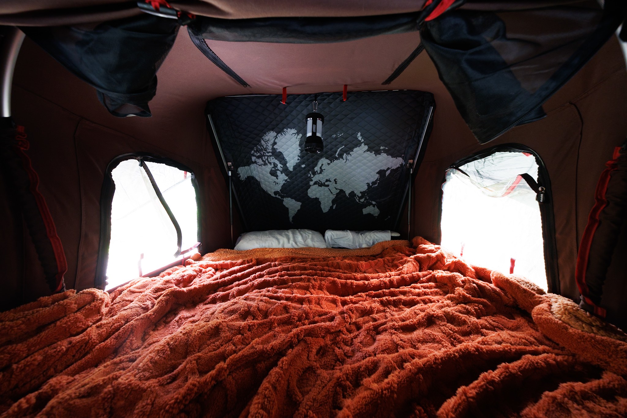 Comfortable sleeping area within an RV rental tent. Features a soft orange blanket, pillows, and a world map wall decor.. Oregon Trail'r TerraDrop Alpha 2024