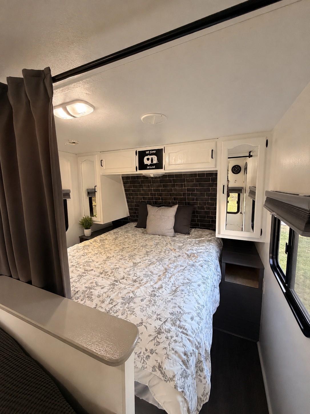 RV rental interior: A cozy bedroom with a floral bedspread, dark brick accent wall, white cabinets & separating curtain.. Keystone RV Springdale 5K 2010