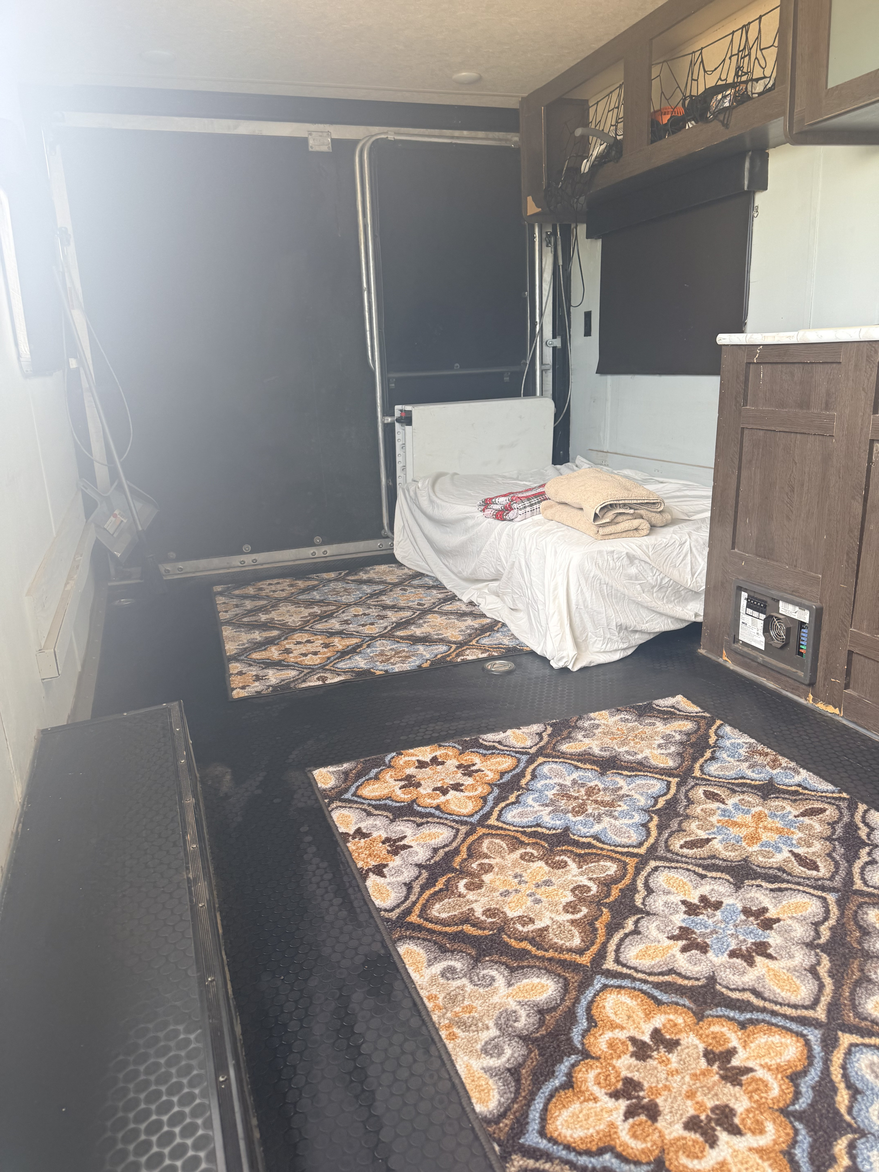 RV rental interior: a toy hauler bedroom with a fold-down bed, patterned rugs on black textured flooring, and overhead storage.. Forest River Salem FSX Toy Hauler 2019