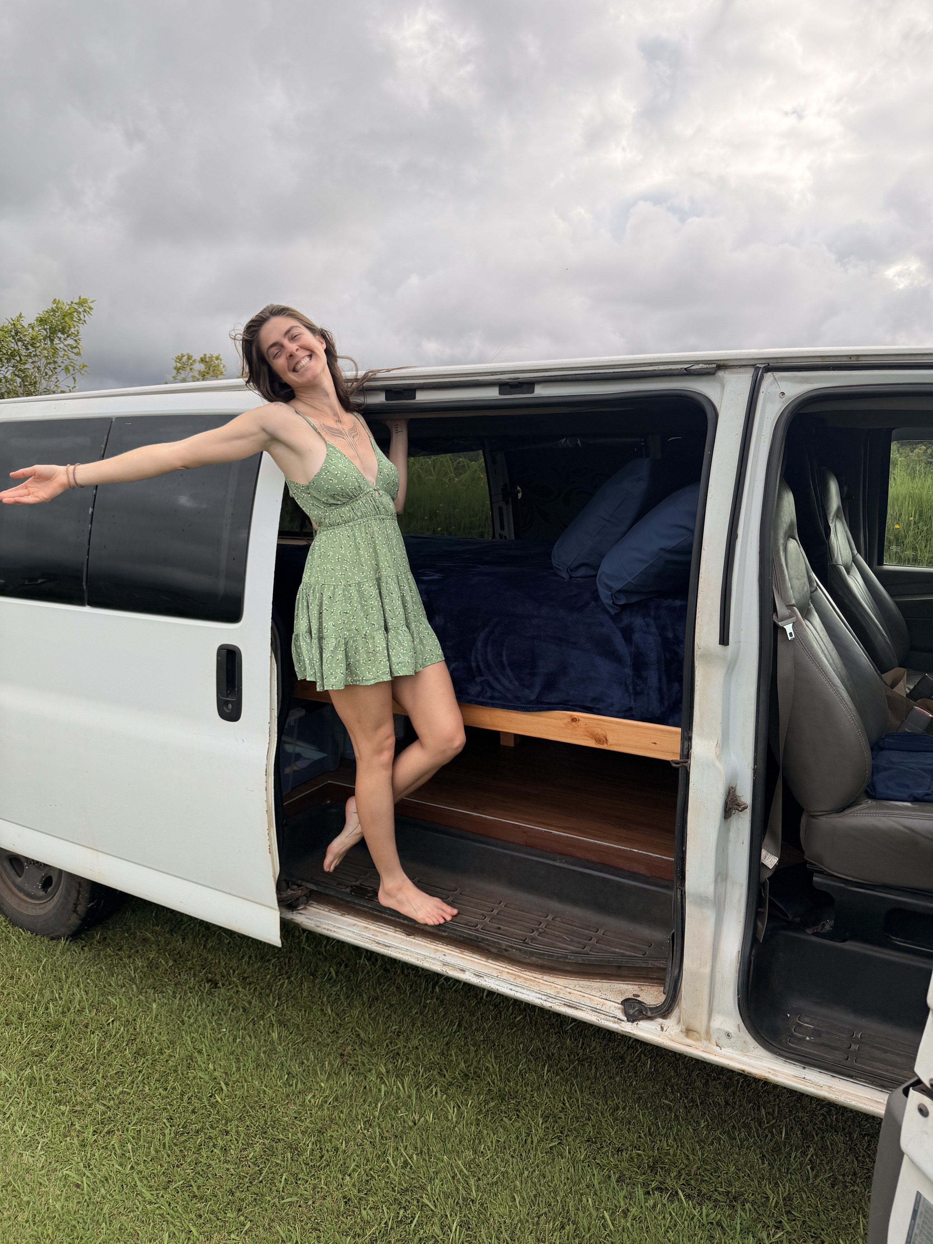 Smiling woman in a green dress stands by her cozy rv rental van, showing the bed inside. Ready for van life and travel adventures.. Chevrolet Express 3500 extenses 2009