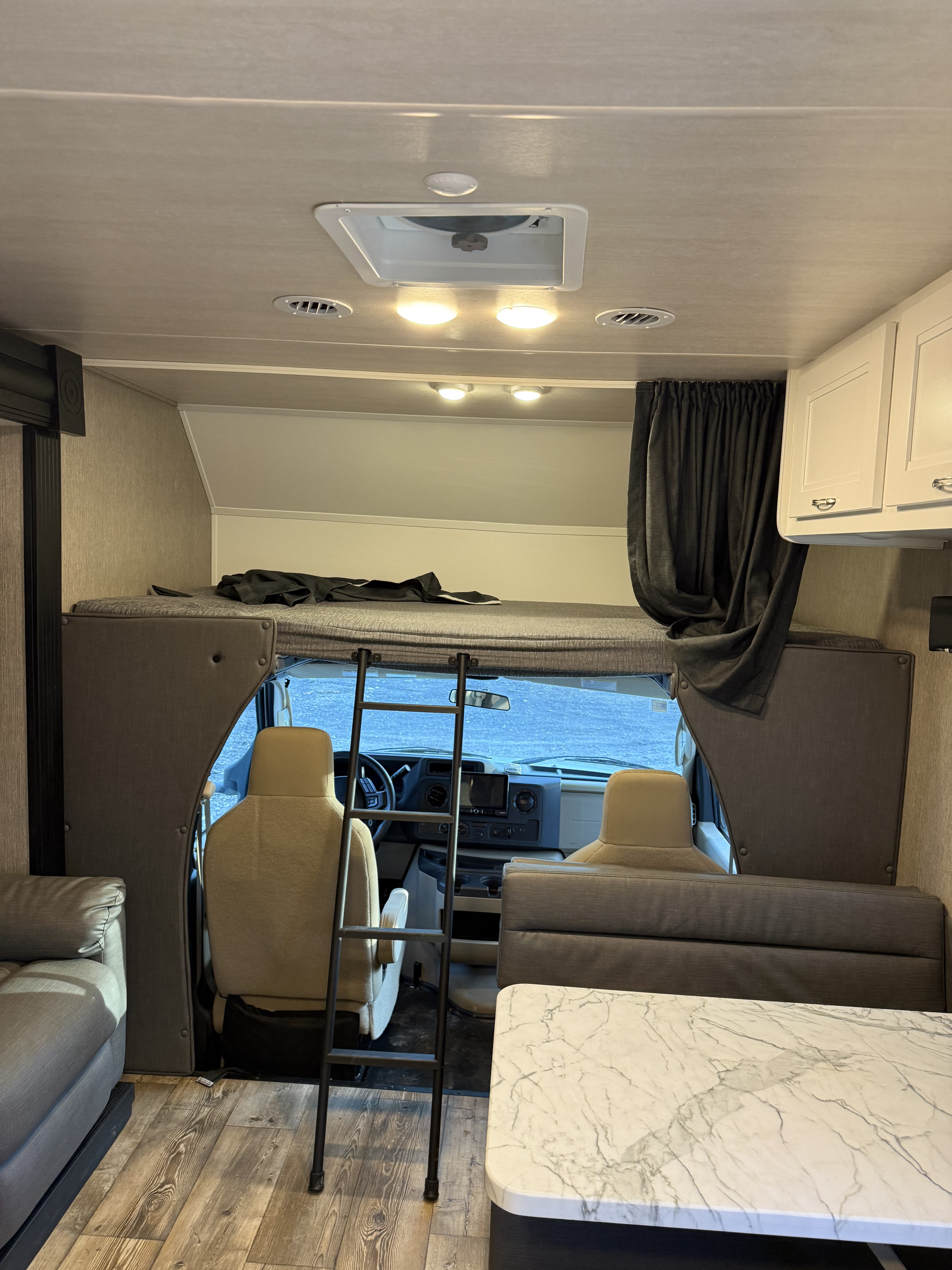 Cozy rv rental interior with a bunk bed, dinette, and cockpit visible. Ready for adventure!. Nexus RV Triumph 2023