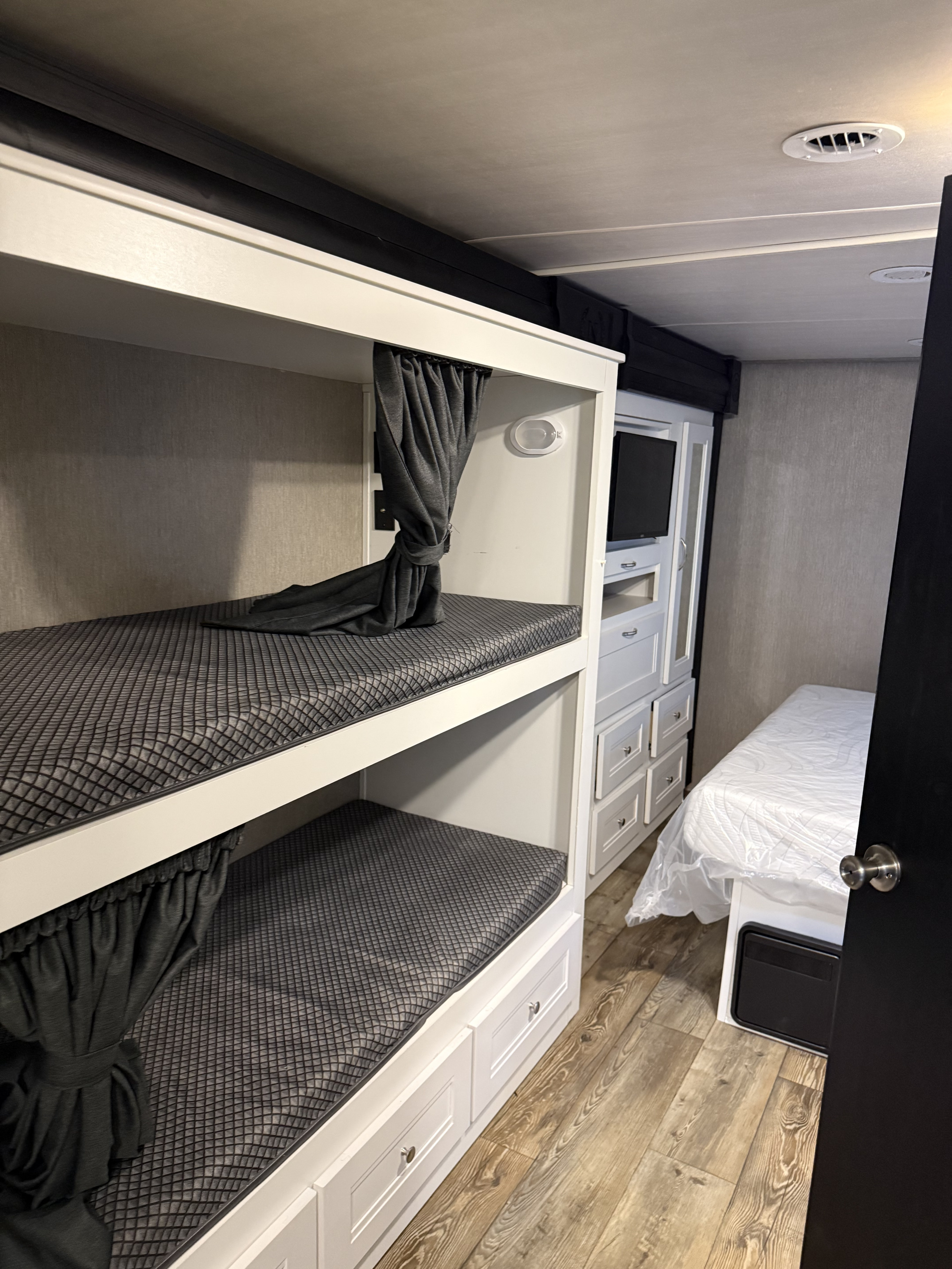 RV rental interior features bunk beds with grey mattresses/curtains, storage, and a single bed. A compact, functional bedroom space.. Nexus RV Triumph 2023