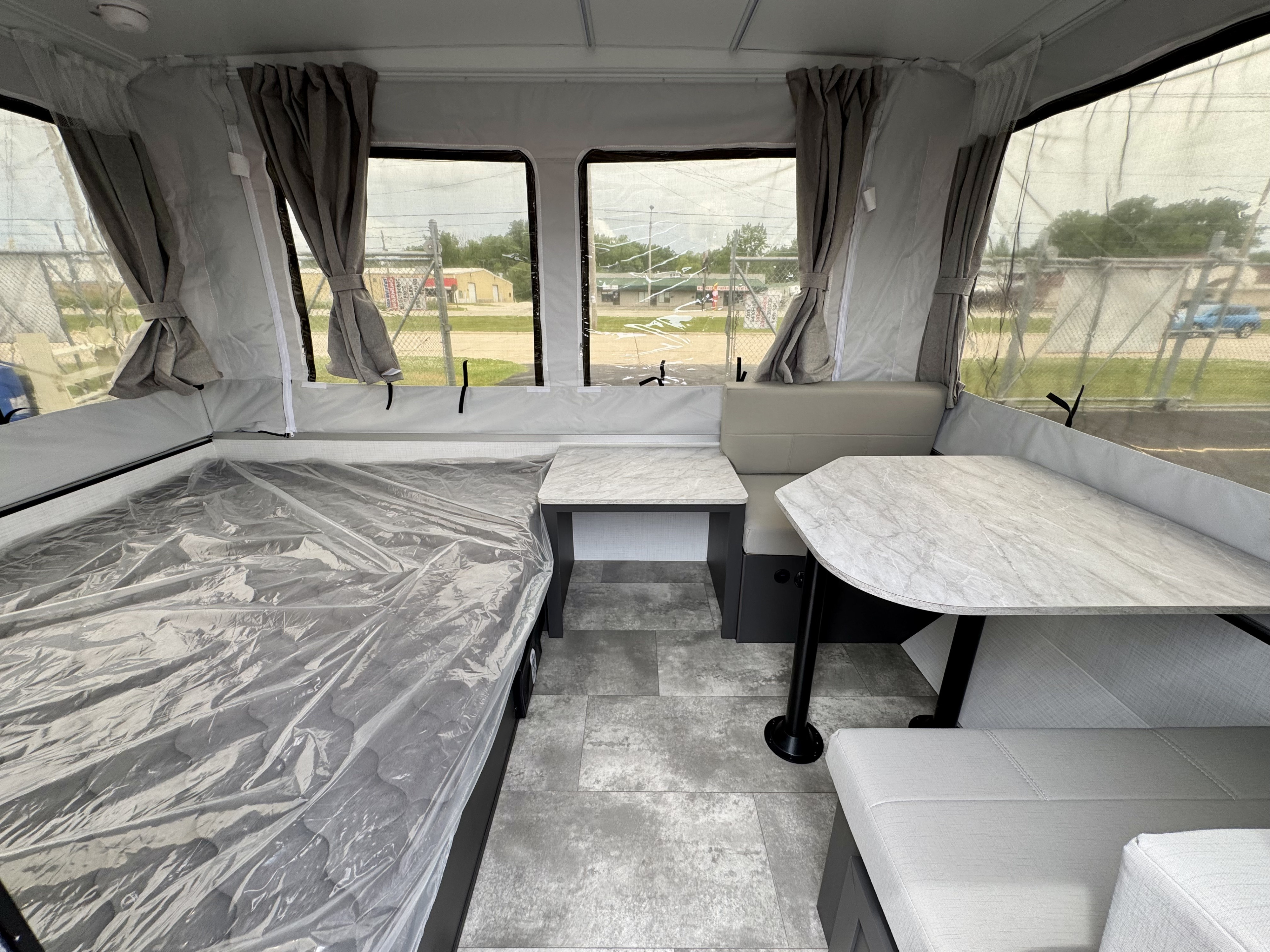 Bright pop-up RV rental interior, featuring a plastic-covered bed, dinette, and tables in a gray modern style.. Forest River OTG 2025