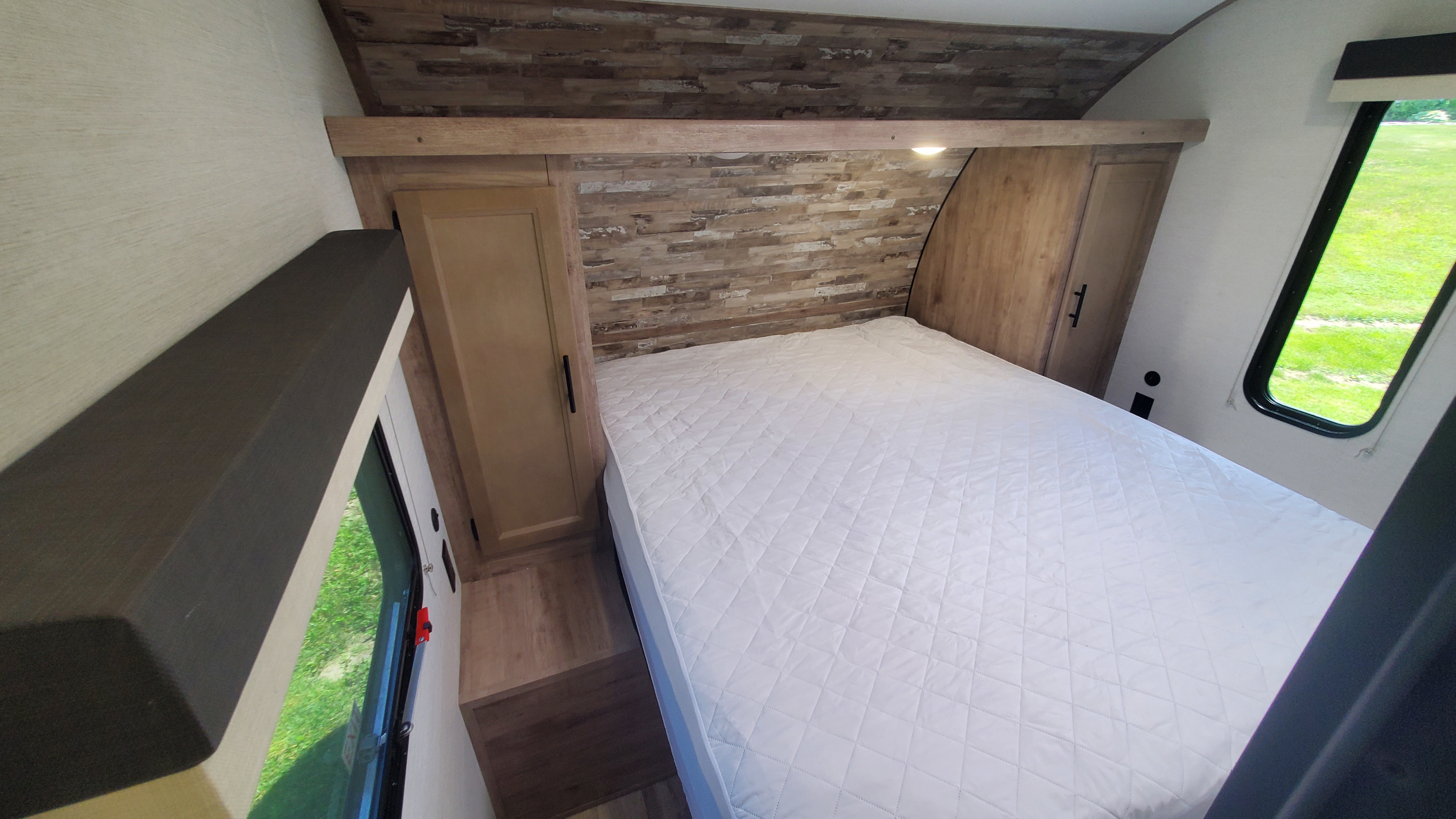 Spacious RV rental bedroom with a comfy white bed, modern wood accents, and convenient storage for your travels.. Gulf Stream Ameri-Lite 2024