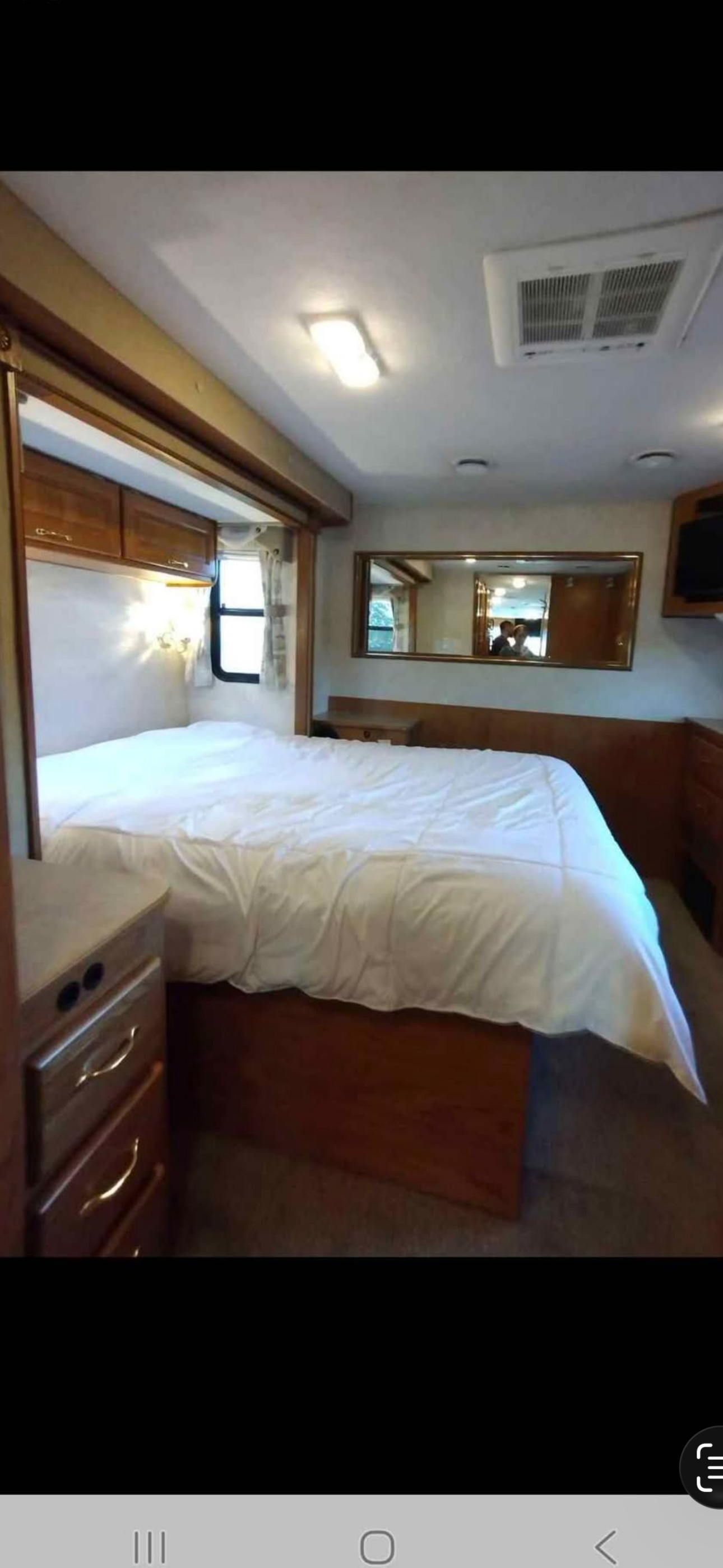RV rental bedroom featuring a clean bed, wooden cabinetry, and a wall mirror. Explore comfortably on your next journey.. Ford 1F6NF3S740A06630 2004