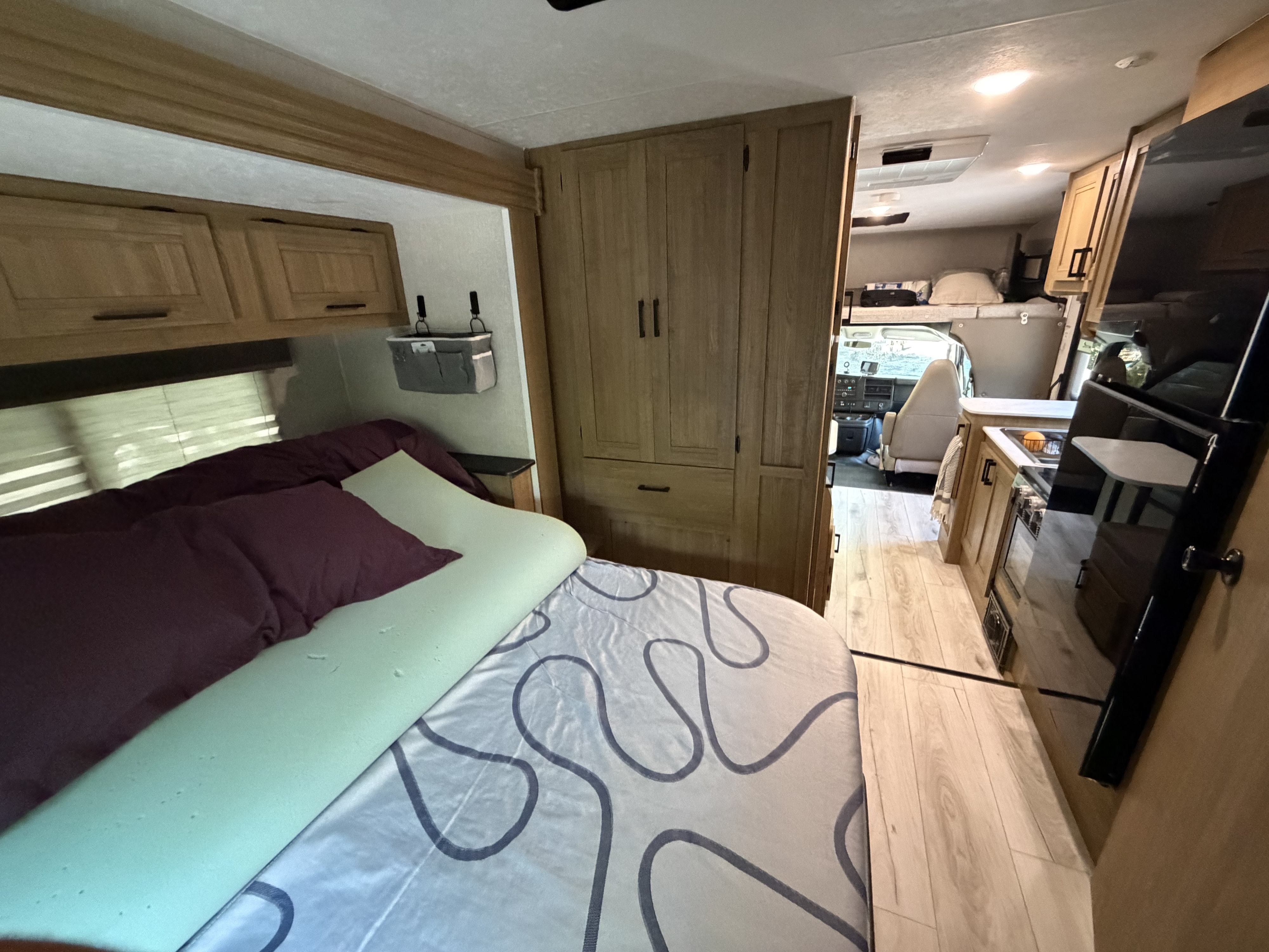 RV rental interior, showcasing the bedroom with topper, built-in storage, kitchen, and front driving area.. Coachman Leprechaun 2025