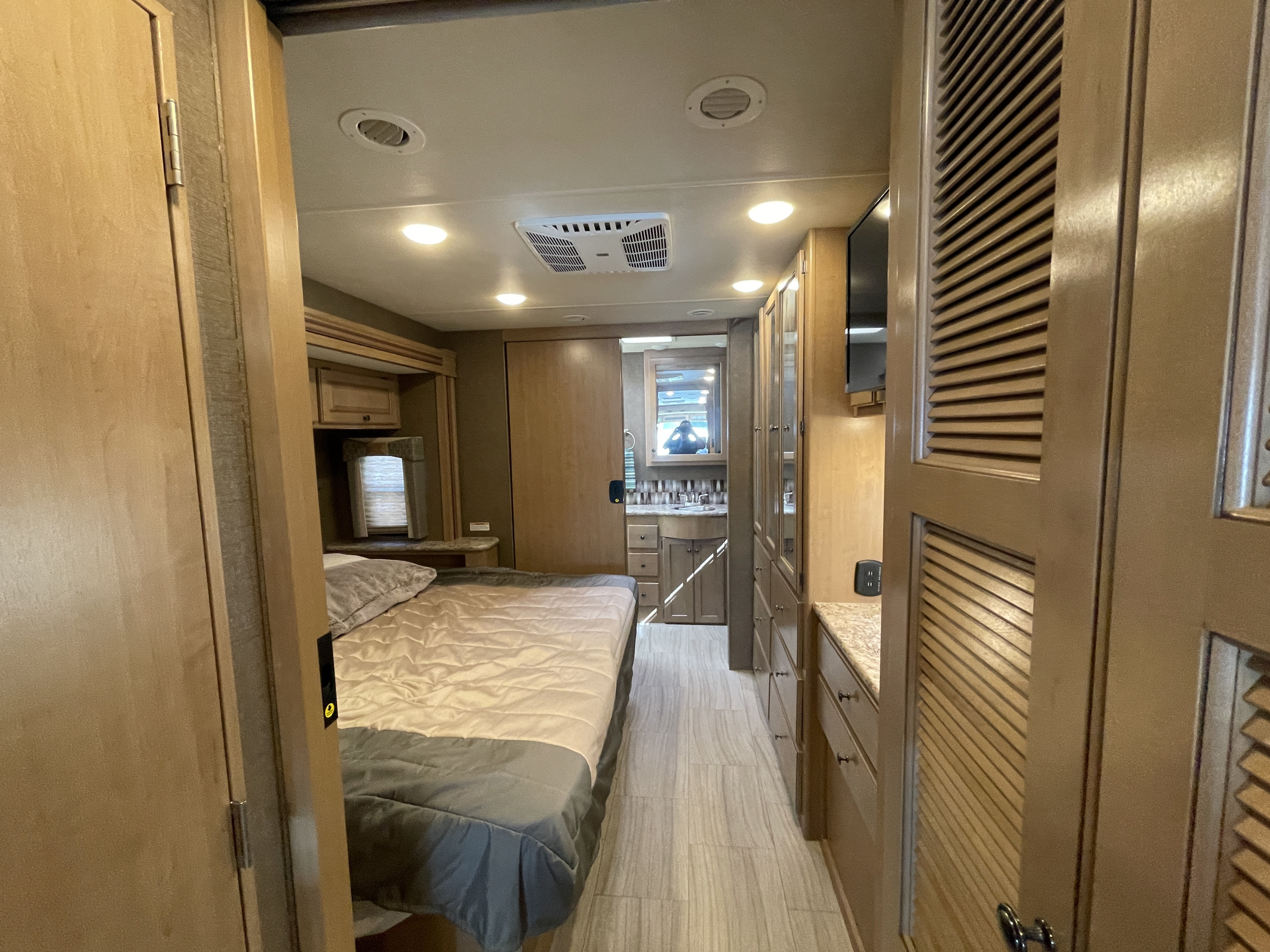 Modern RV rental interior: A comfortable bedroom leads to a hallway with storage, a wall-mounted TV, and a bathroom vanity.. Thor Windsport 2019