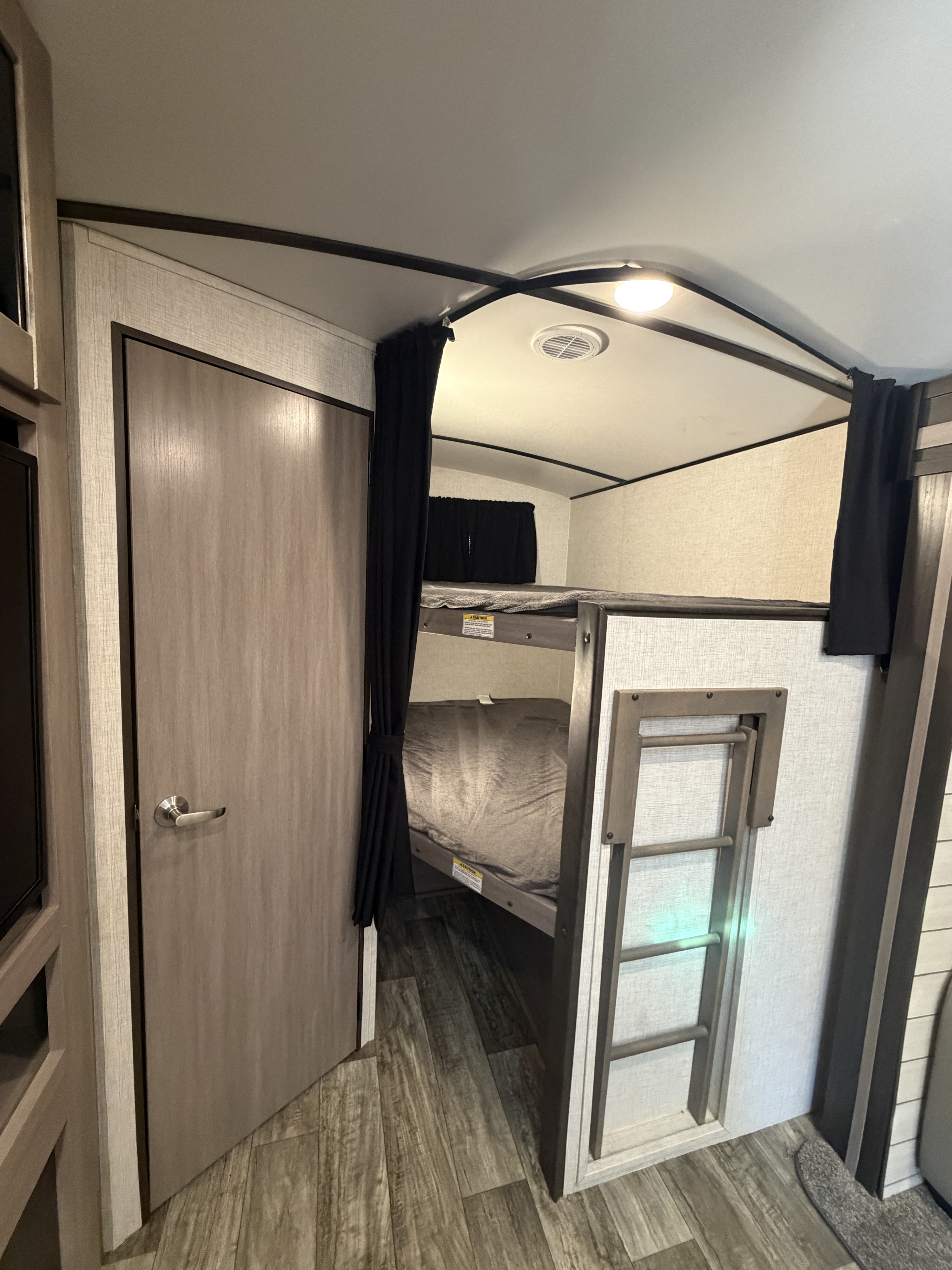 Inside an rv rental: a cozy bunk bed area with privacy curtains, a sturdy ladder, and a closed door, ideal for compact living.. Crossroads RV Sunset Trail Super Lite 2021