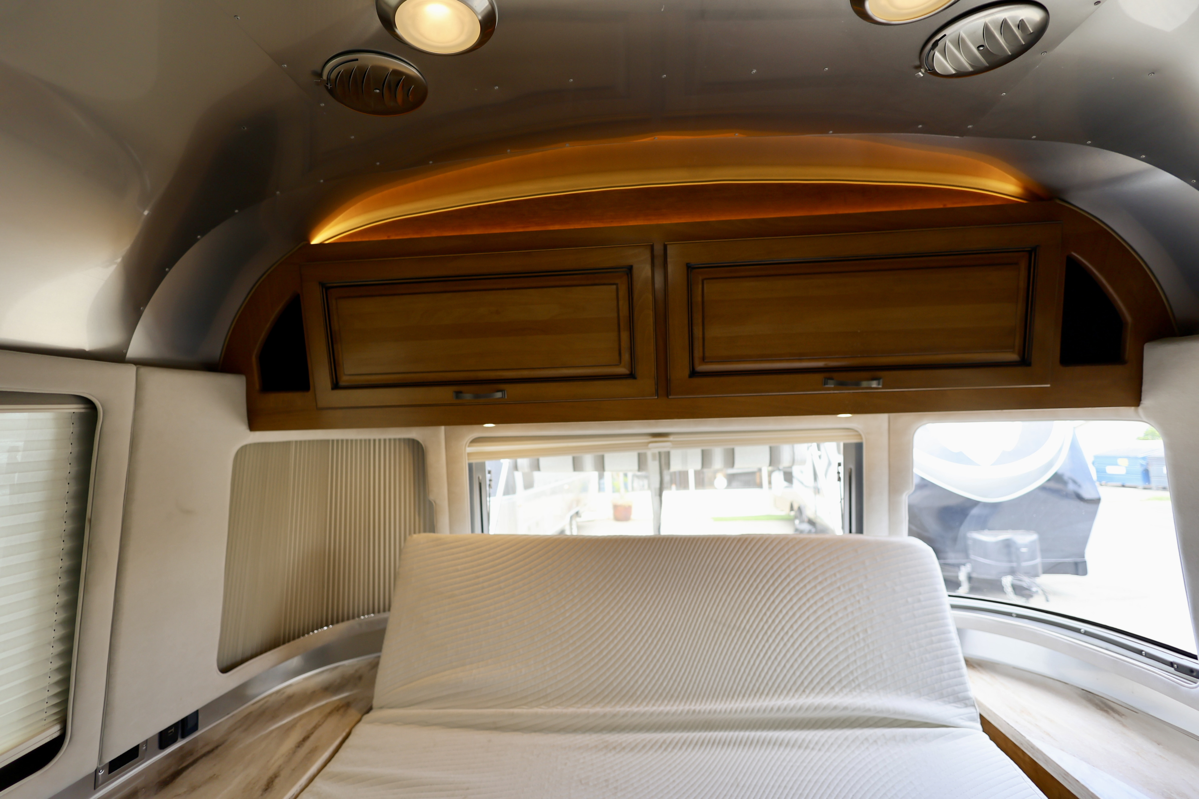Modern RV rental interior with a curved, polished metal ceiling, warm overhead lighting, wooden cabinets, and a cozy bed.. Airstream Classic 2019