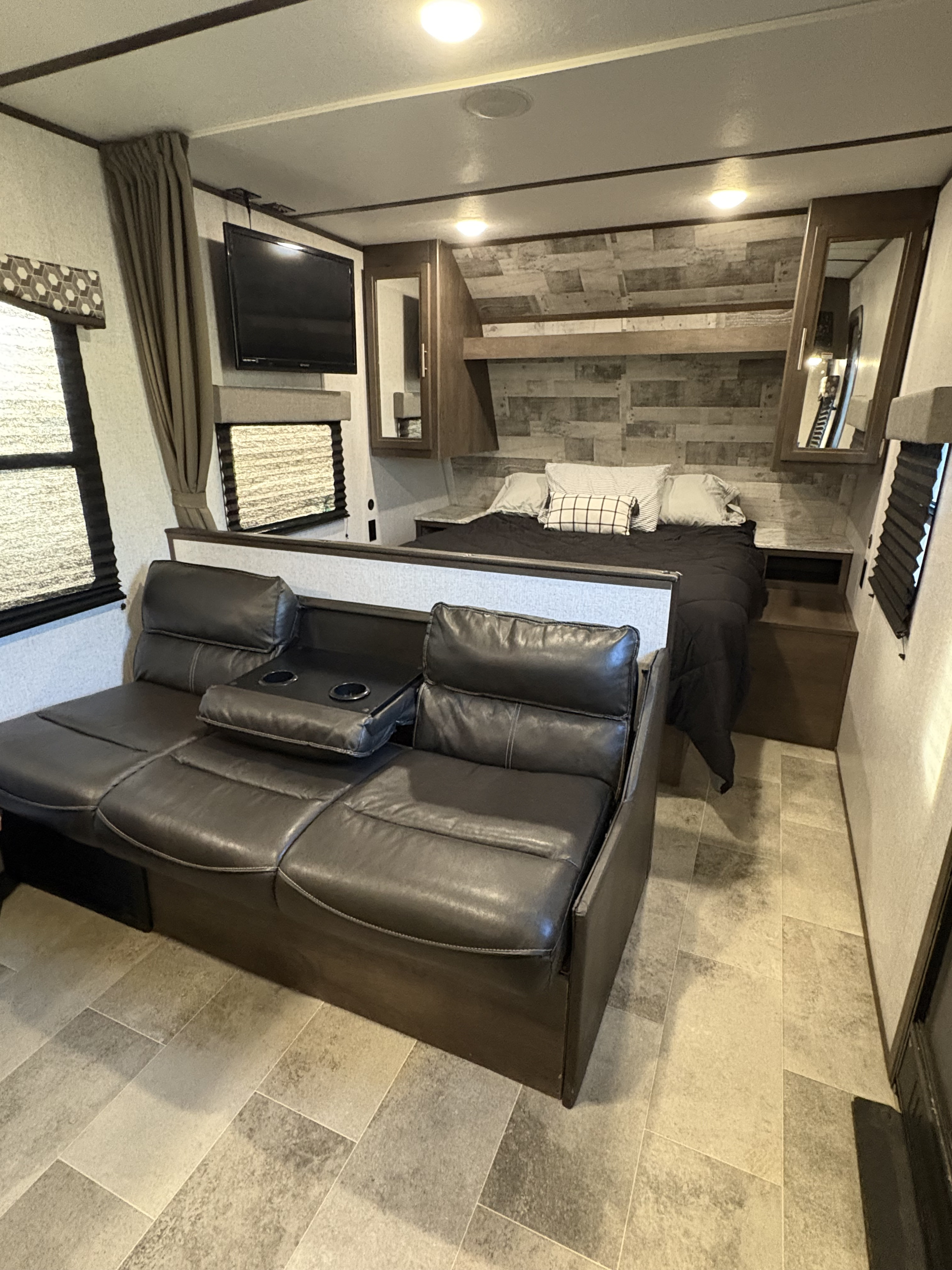 RV rental interior: a compact living and sleeping area with a dark gray leather sofa, queen bed, and TV.. Dutchmen Coleman Lantern LT 2020