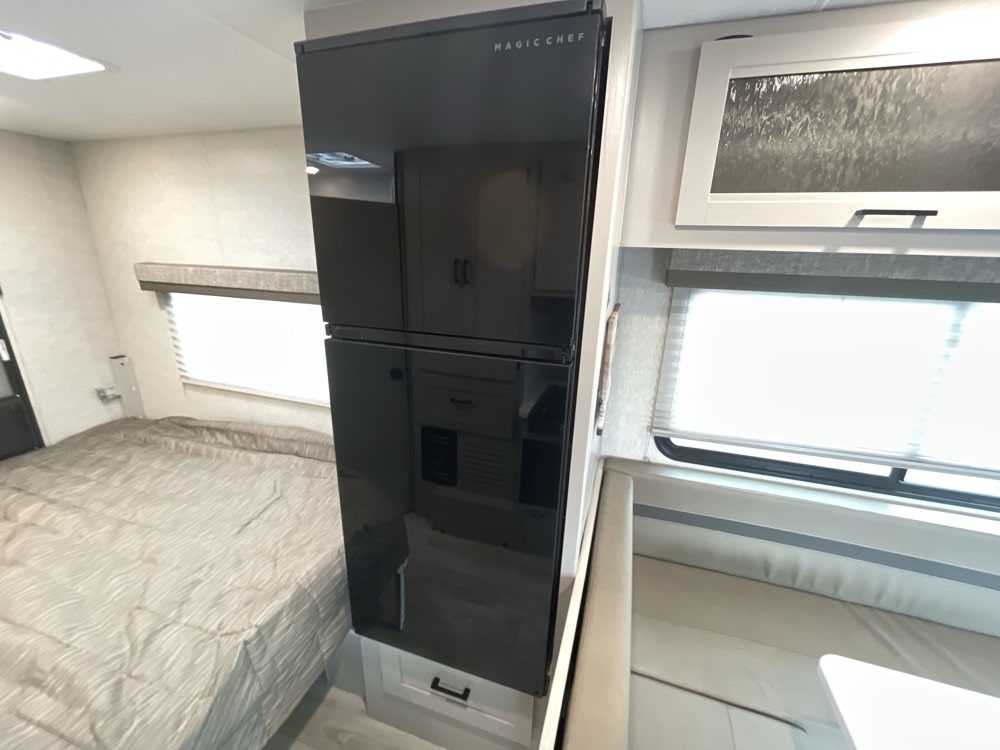 Modern RV rental interior with a sleek black Magic Chef refrigerator, a cozy bed, and a comfortable dinette.. Coachmen Freelander 22xg 2024