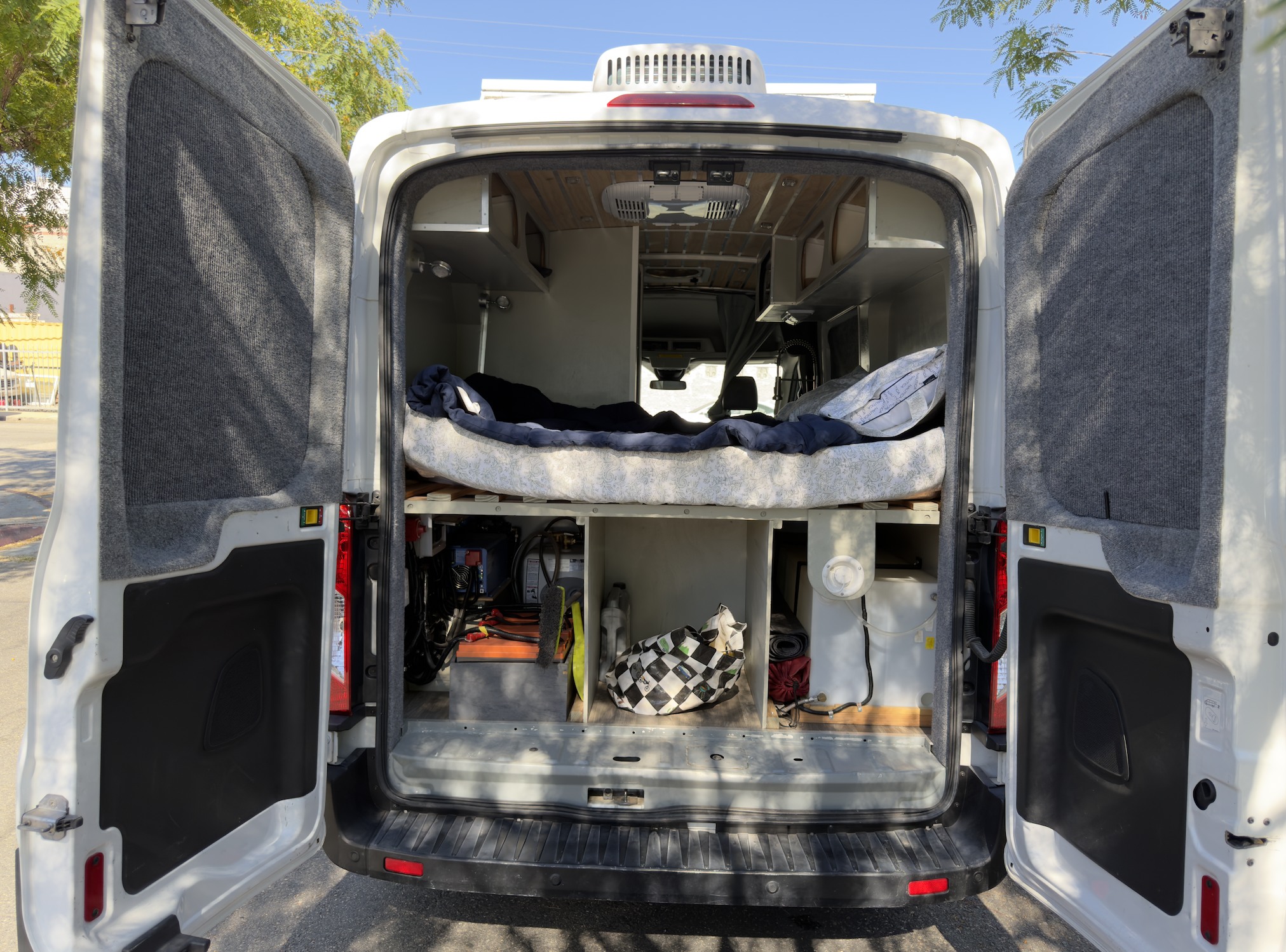 RV rental camper van's custom interior: open rear doors show a raised bed, storage, and utility setup.. Ford Transit 2017