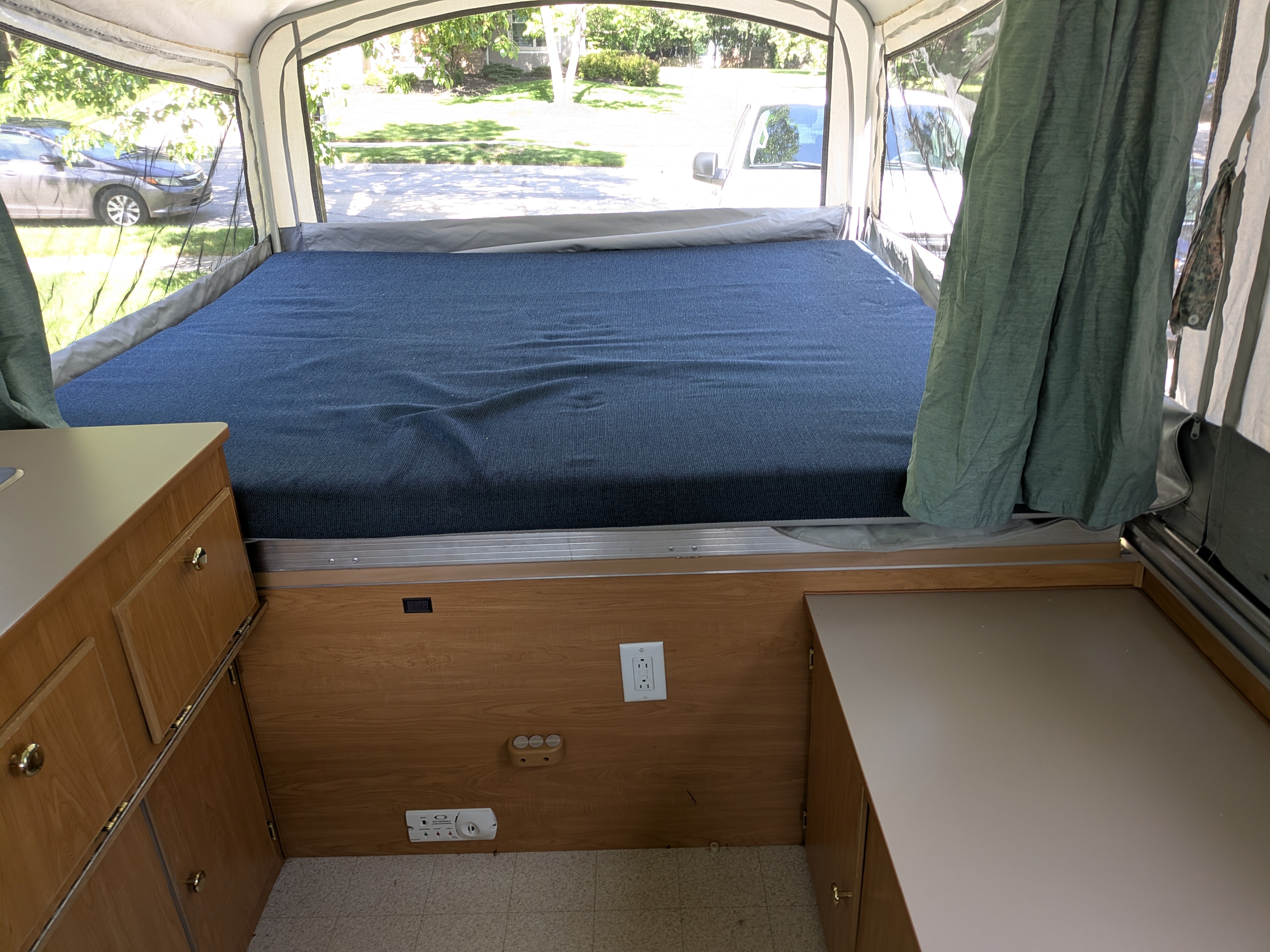 An RV rental's pop-up interior shows a large bed, cabinetry, and views of a neighborhood through its mesh windows.. Coleman Destiny Sedona 2002