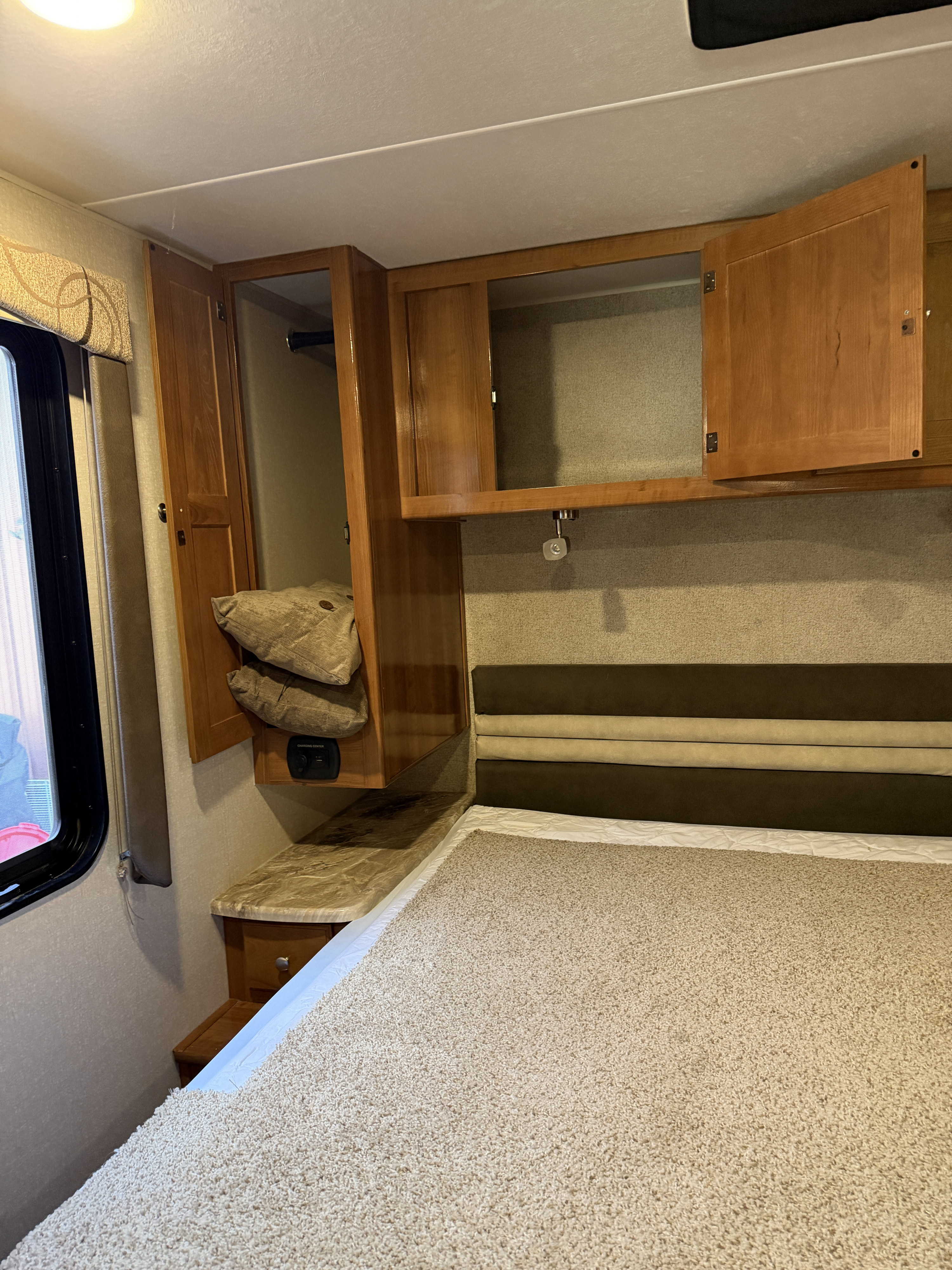 Cozy RV rental bedroom with a bed, upholstered headboard, wood cabinets, and a convenient charging center.. Coachman Coachman Leprachaun 319MB 2019