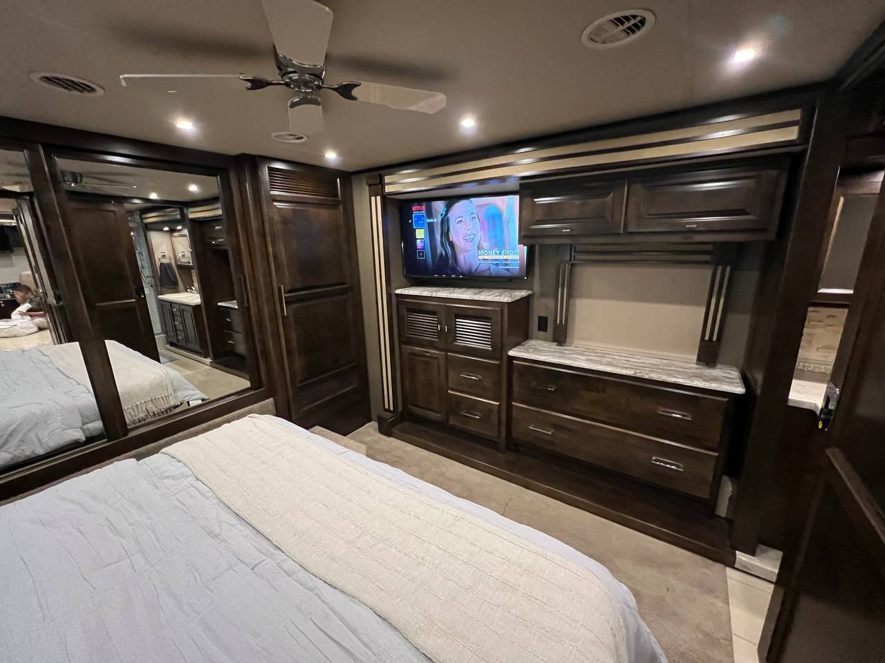 Inside a premium RV rental: a cozy bedroom with TV, ample storage, and full-length mirrors reflecting a bathroom vanity.. Allegro Allegro Red 2019