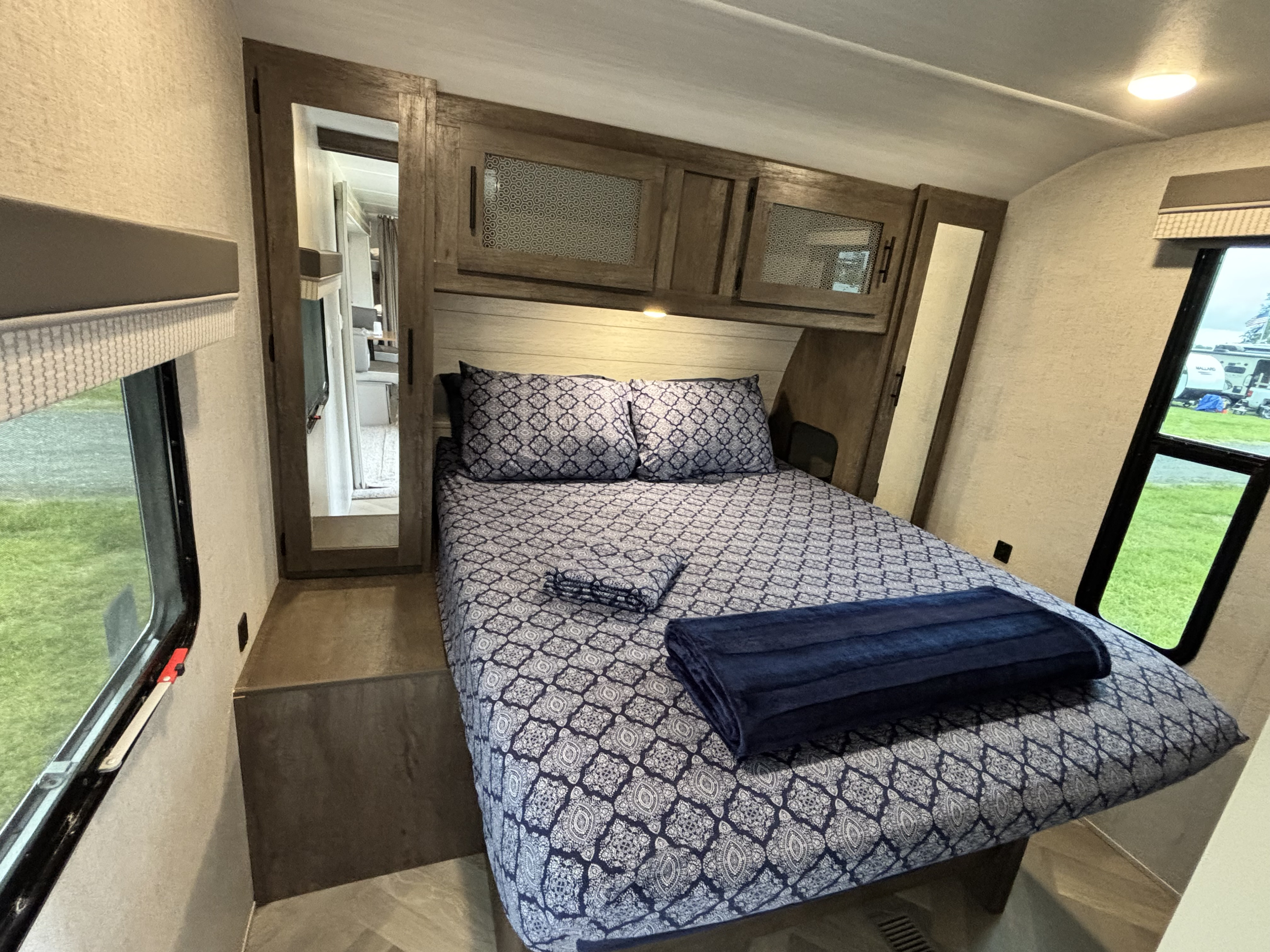 This cozy RV rental bedroom features a patterned bed, storage cabinets, and large windows, perfect for comfortable travel.. Forest River Wildwood 2021
