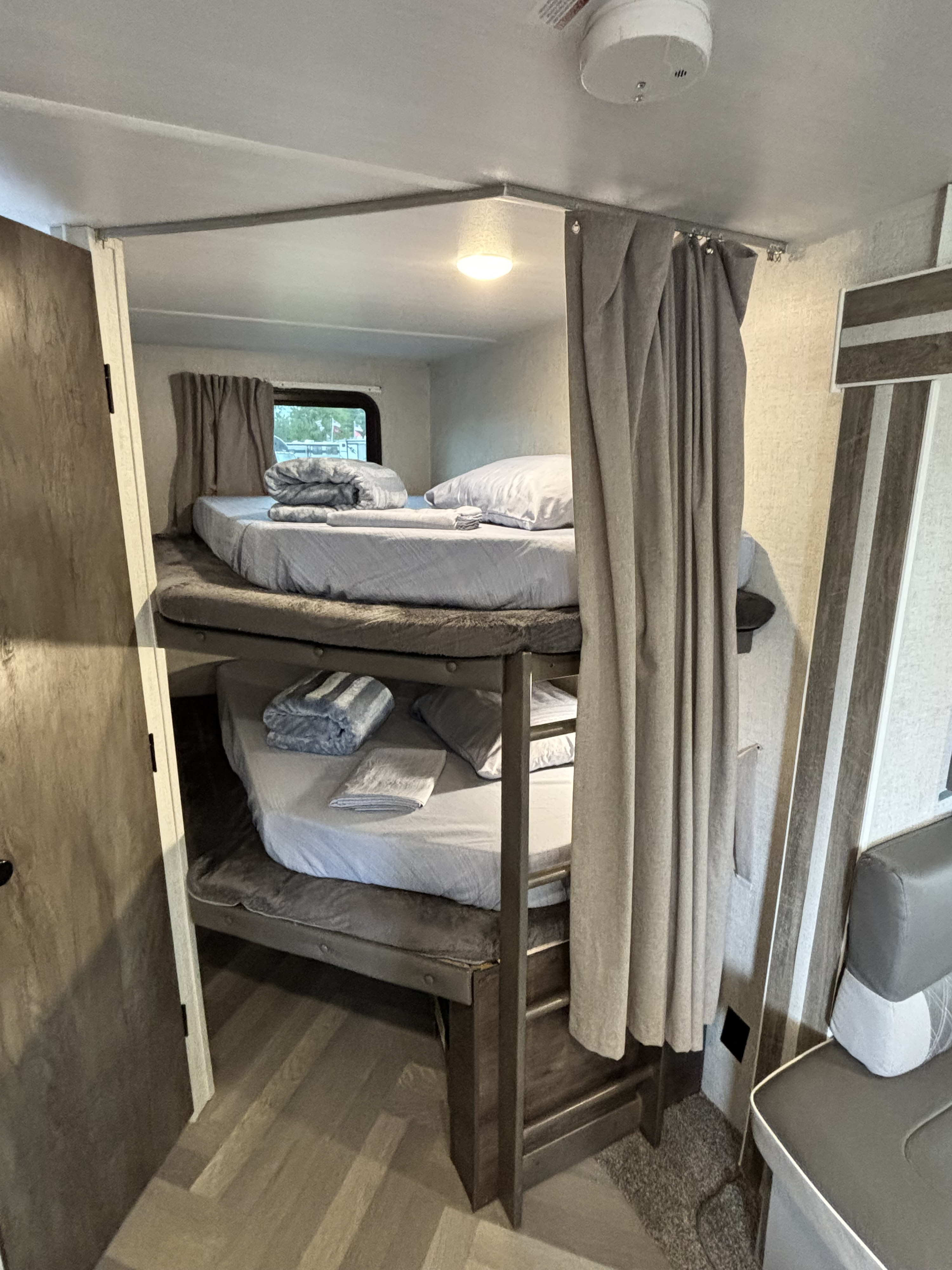Cozy bunk beds in an rv rental, featuring light gray bedding, privacy curtains, and a window for comfortable sleeping space.. Forest River Wildwood 2021