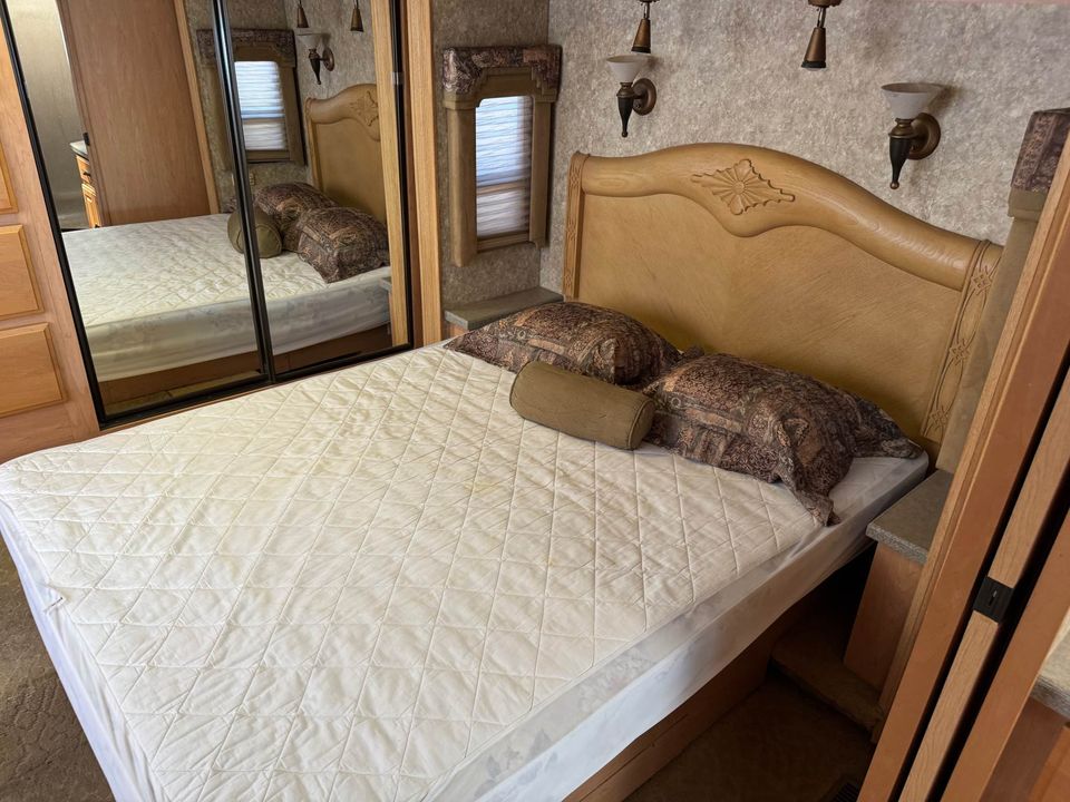 Cozy RV rental bedroom featuring a bed with quilted mattress, wooden headboard, pillows, and a mirrored closet.. Coachmen Sportscoach Encore 2005