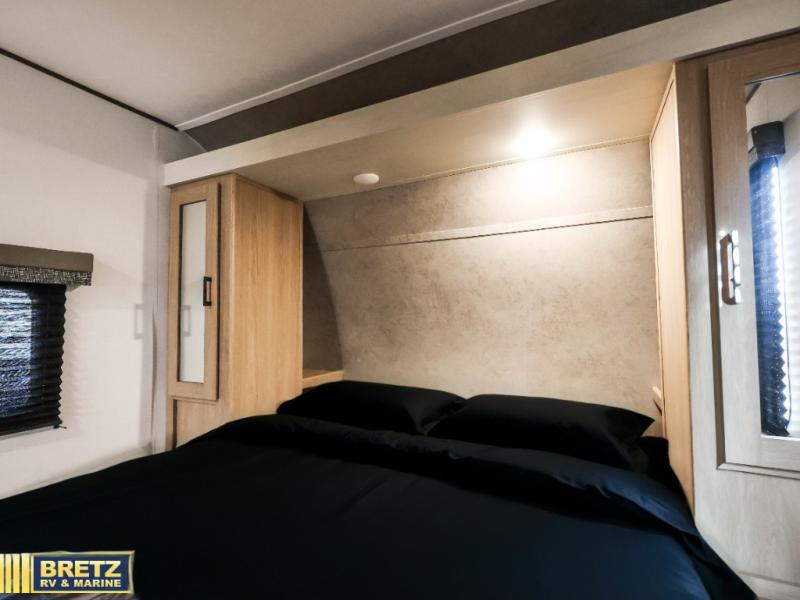 This modern rv rental bedroom features a comfortable bed, integrated overhead lighting, and wood-toned storage cabinets.. Keystone RV Other 2026