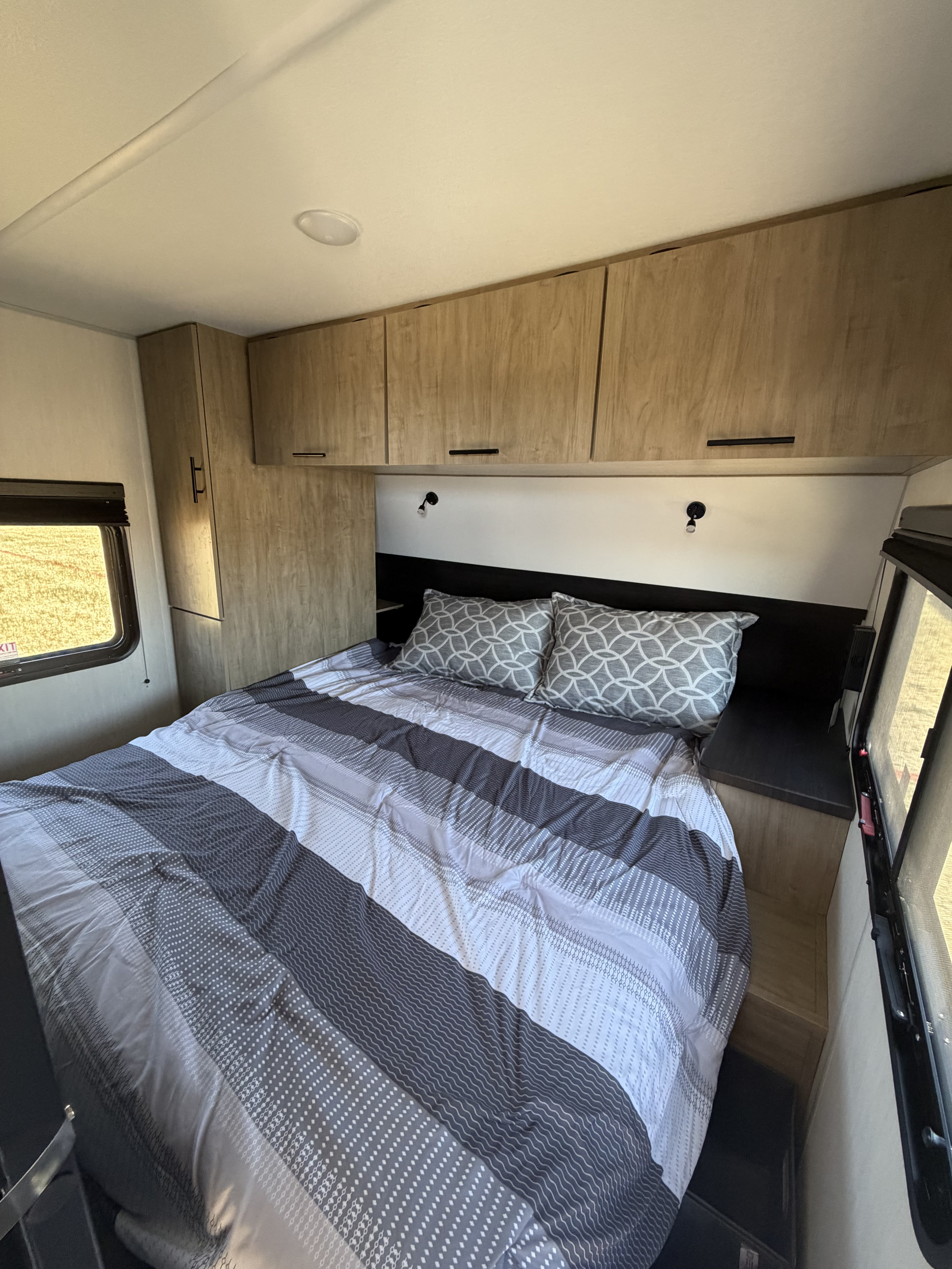 Cozy RV rental bedroom with a striped bed, patterned pillows, storage cabinets, and windows.. Forest River Grey Wolf 26DBHBL 2026