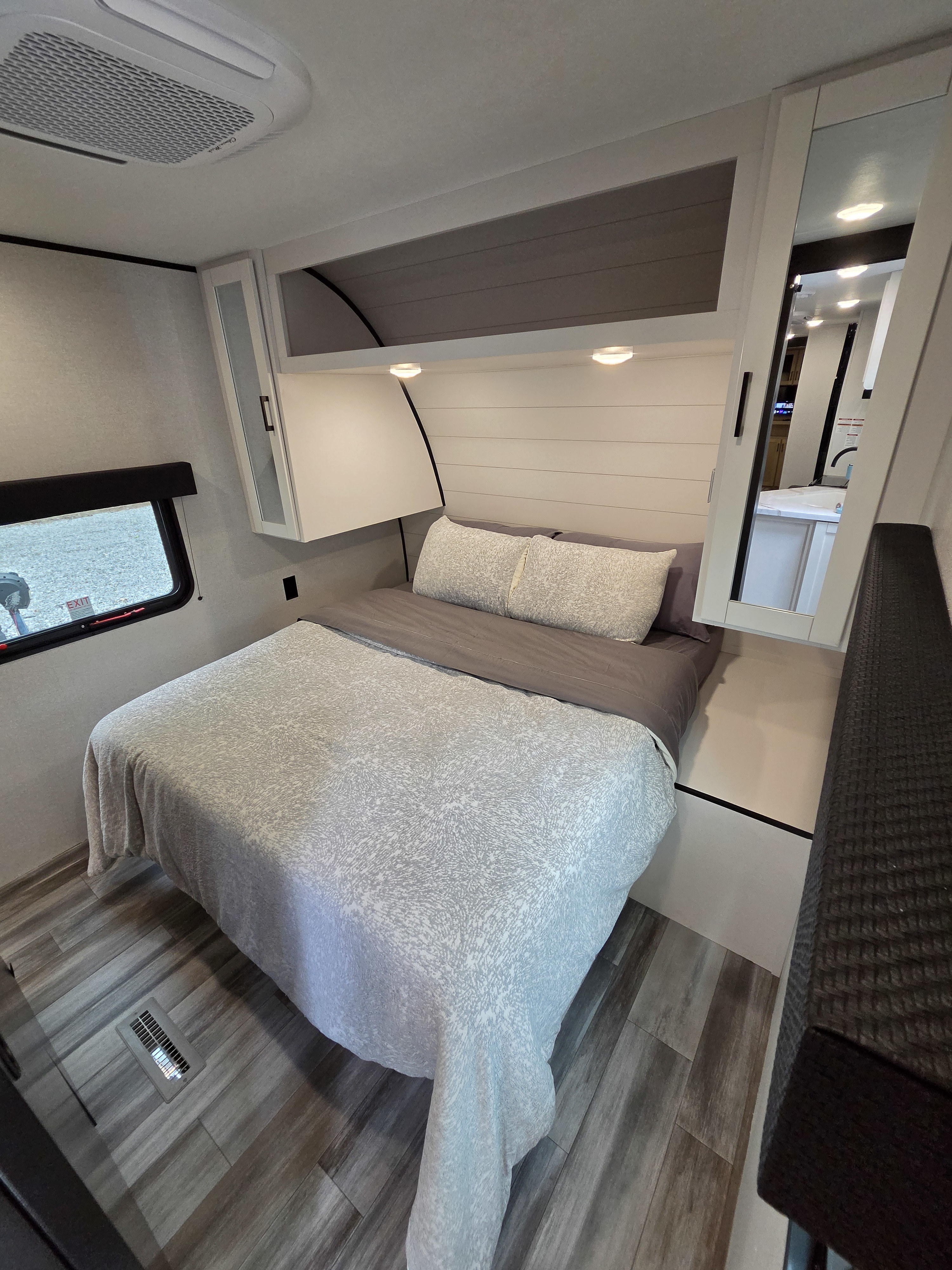 RV rental bedroom with patterned comforter, overhead cabinets, AC unit, window, and wood-look flooring.. Jayco Jay Flight SLX 2025