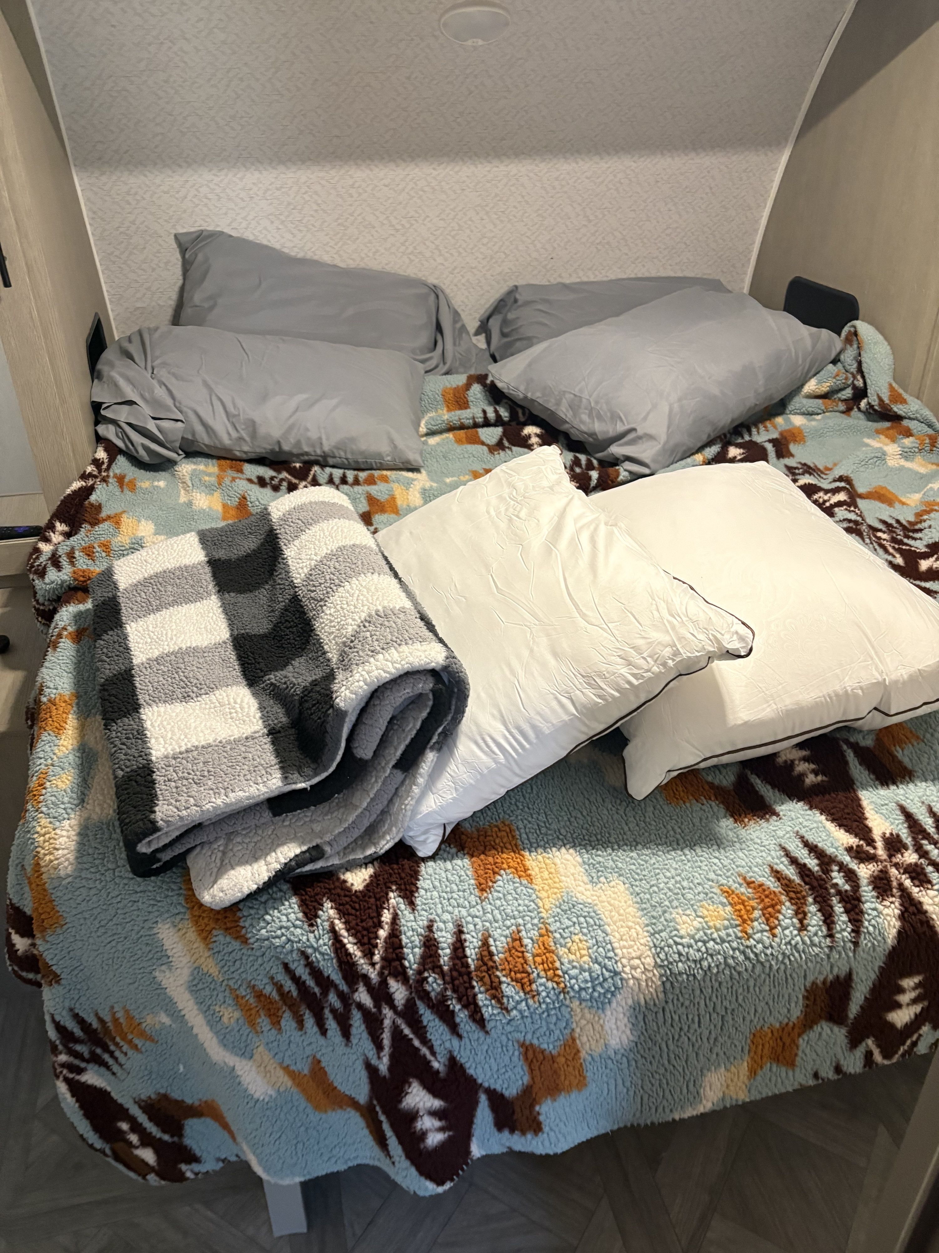 Cozy RV rental bed with grey and white pillows, plus patterned and plaid blankets for a comfortable stay.. Forest River Salem Cruise Lite 2023