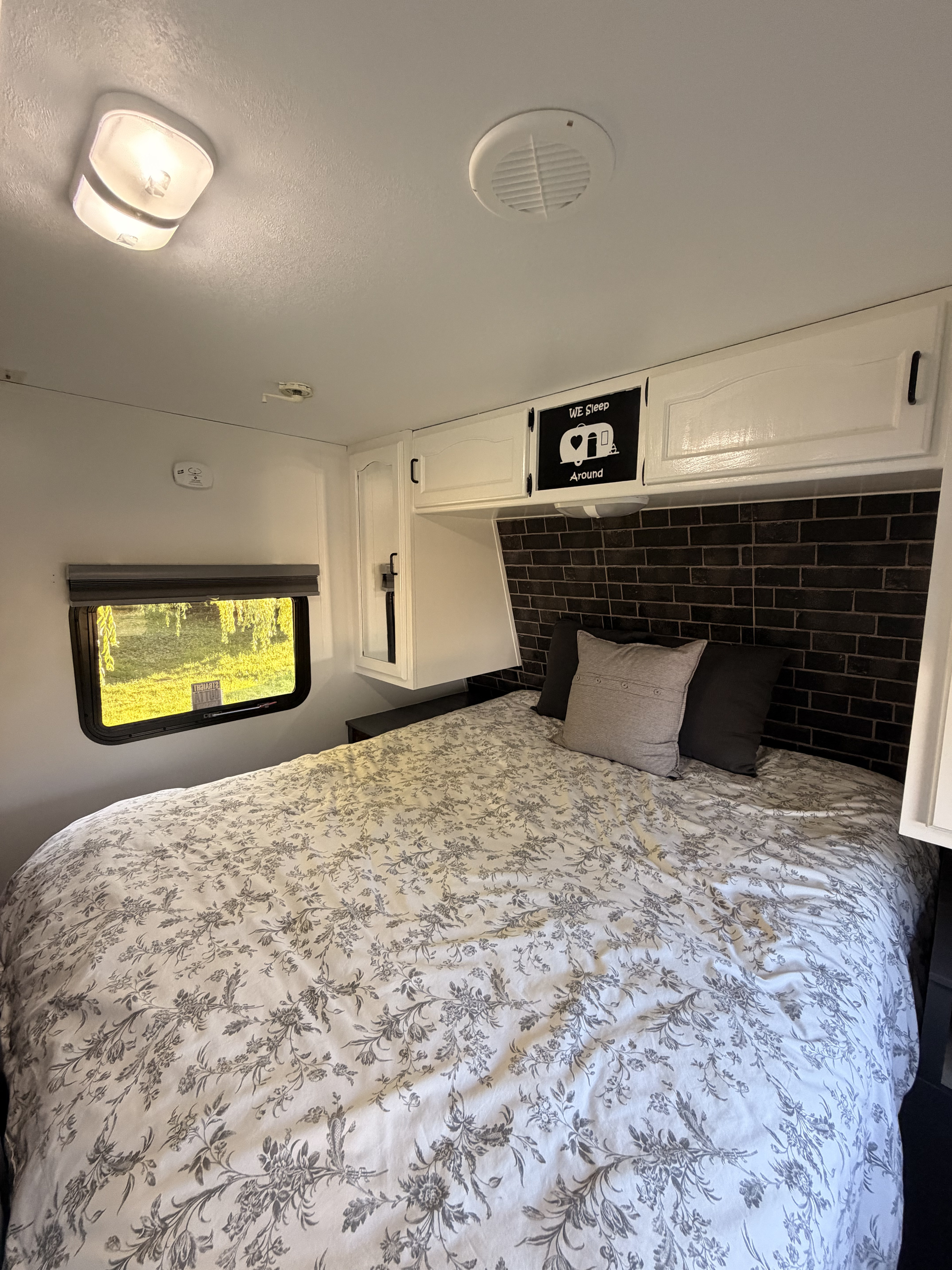 Cozy RV rental bedroom featuring a floral bed, brick accent wall, and a bright window view.. Keystone RV Springdale 5K 2010
