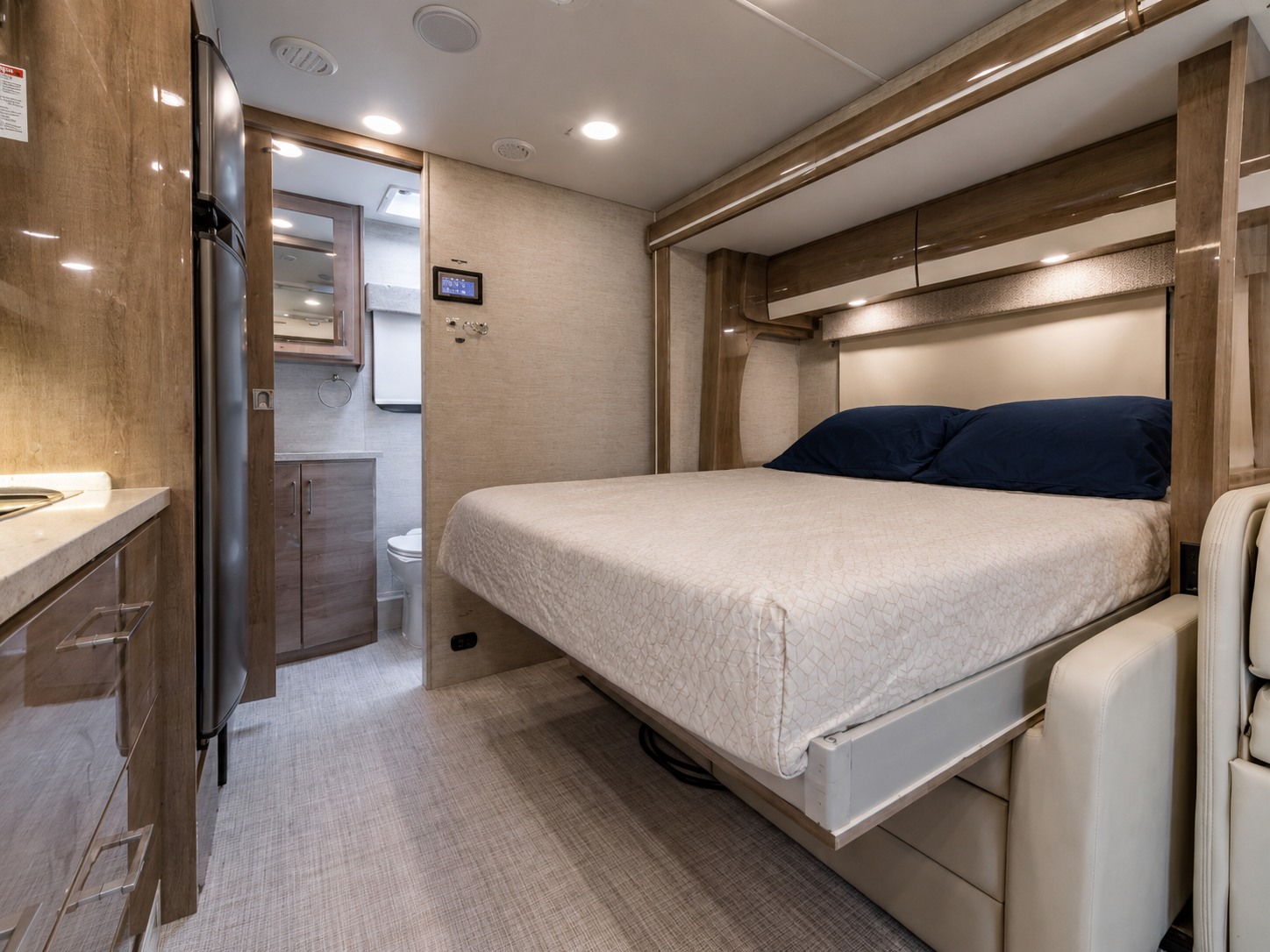 This RV rental interior features a cozy bedroom with a pull-down bed, adjacent bathroom, and kitchen area with a fridge.. Entegra Coach Qwest 2021