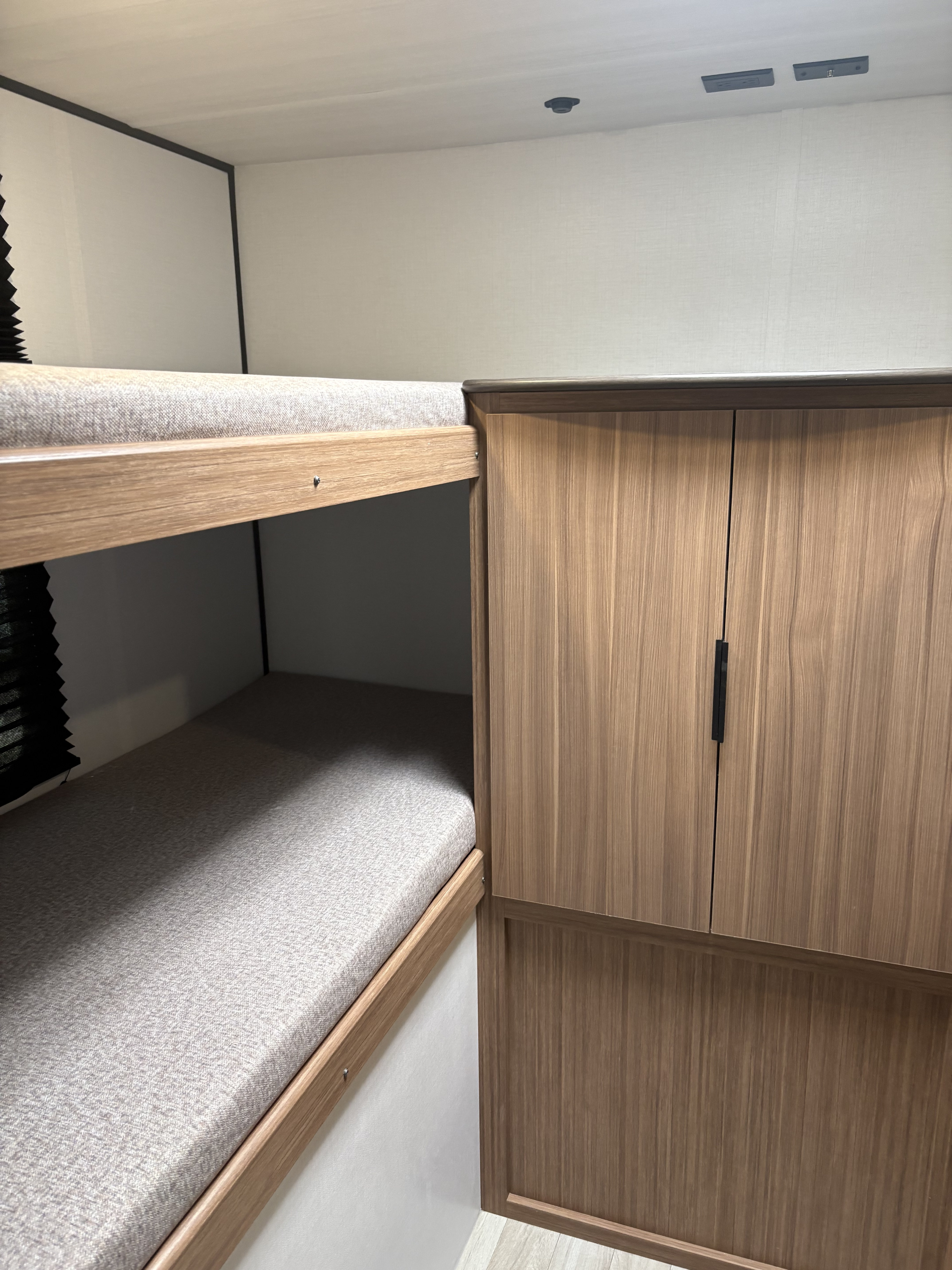 RV rental bunk beds and adjacent wooden storage cabinet. A cozy, compact space with light gray mattresses.. Keystone RV Passport 2026
