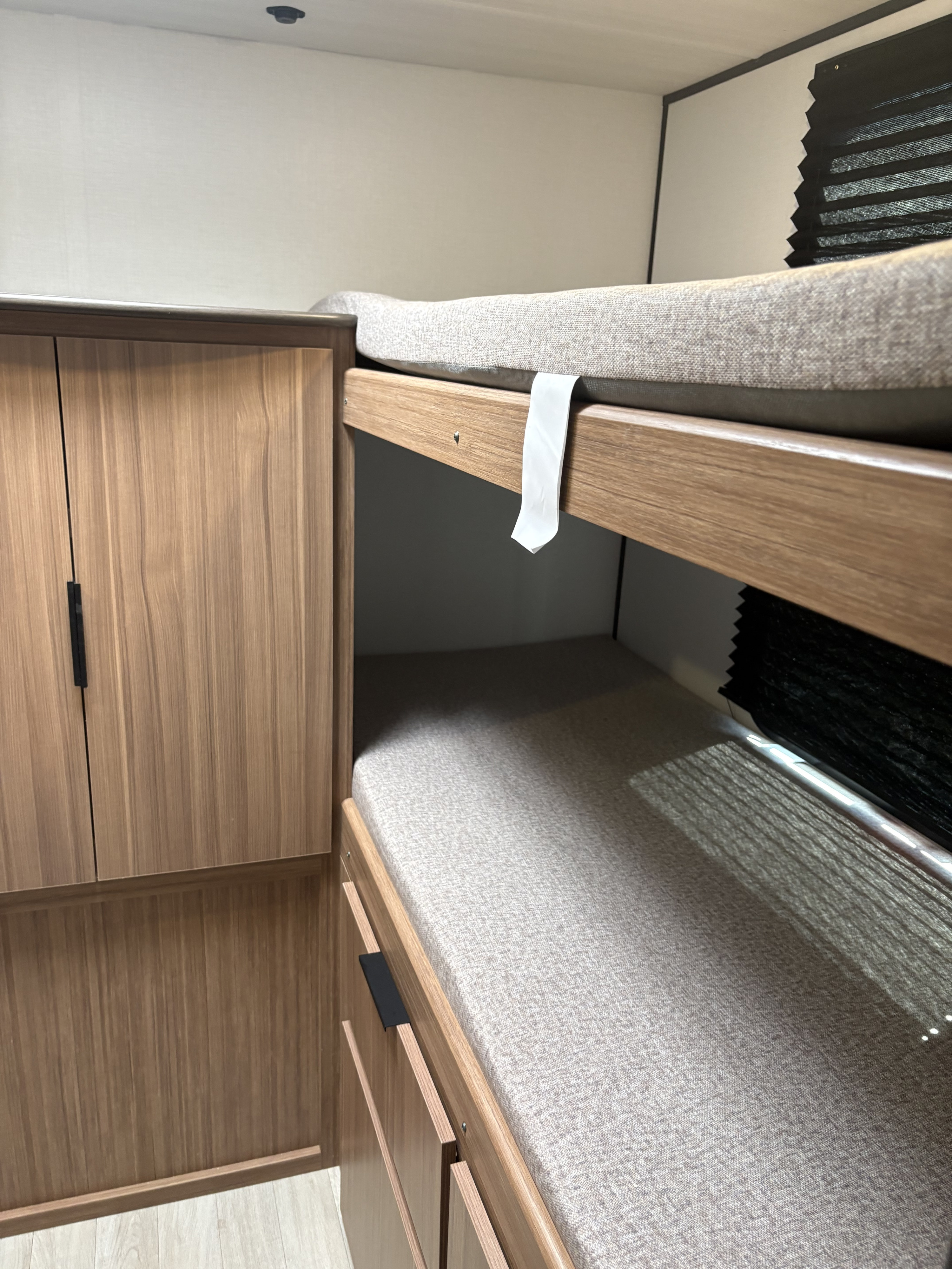 RV rental bunk beds with light gray upholstered mattresses, sleek wood cabinetry, and a black accordion window blind.. Keystone RV Passport 2026