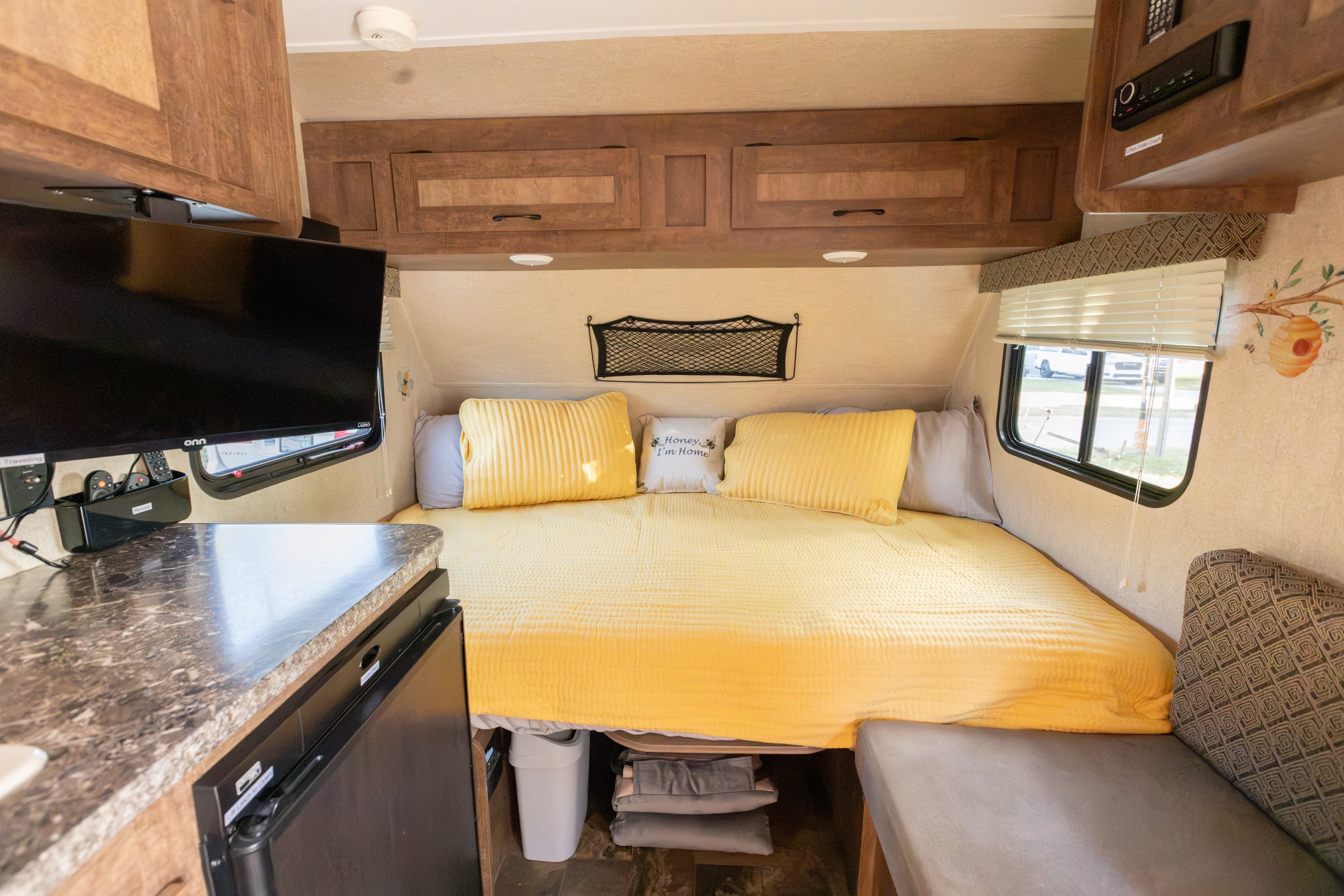 Cozy RV rental bedroom with yellow bedding, mounted TV, overhead cabinets, window, and bee-themed decor.. Starcraft Autumn Ridge Mini 2017