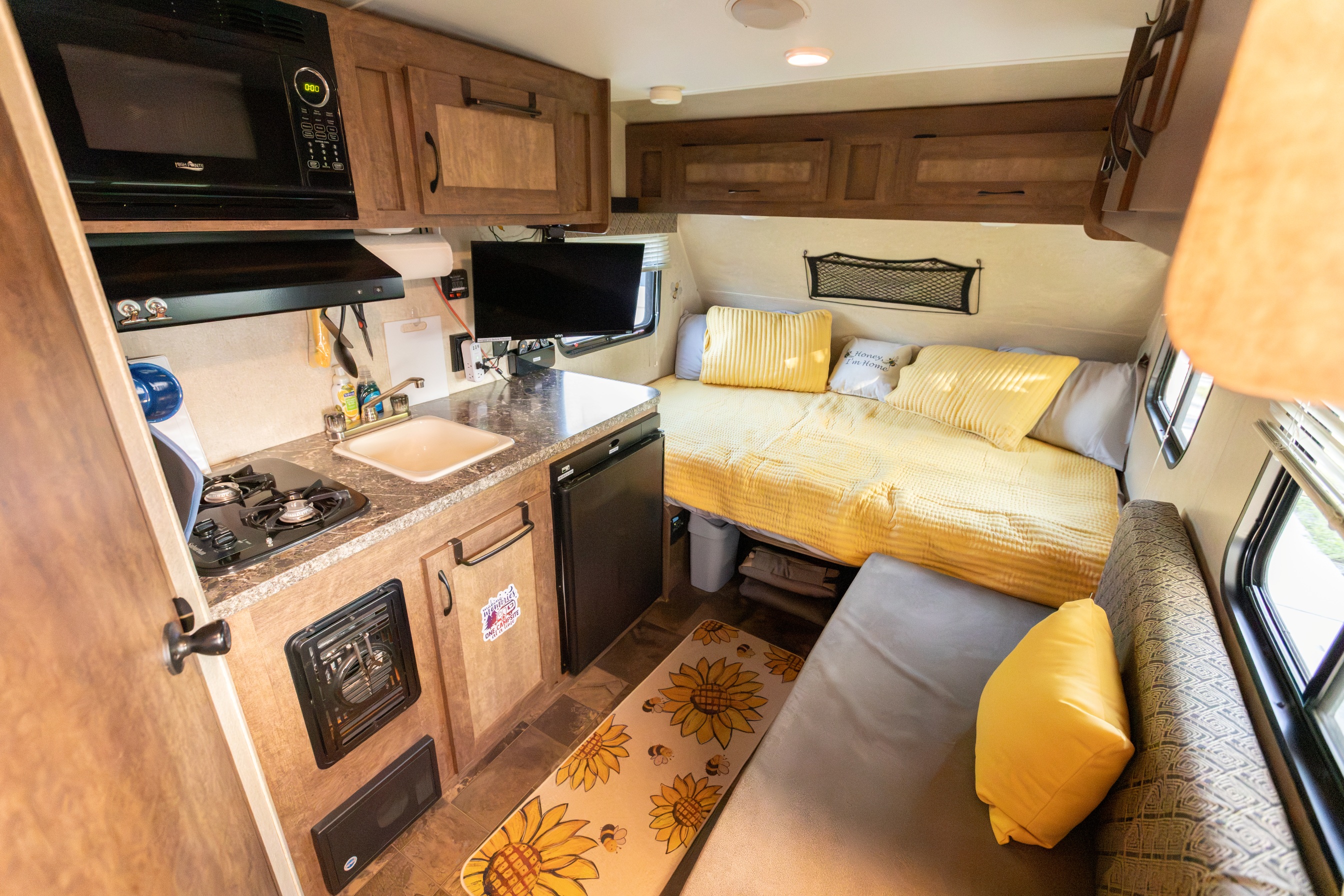Explore this cozy rv rental interior featuring a compact kitchen, bed with yellow bedding, and a small seating area.. Starcraft Autumn Ridge Mini 2017
