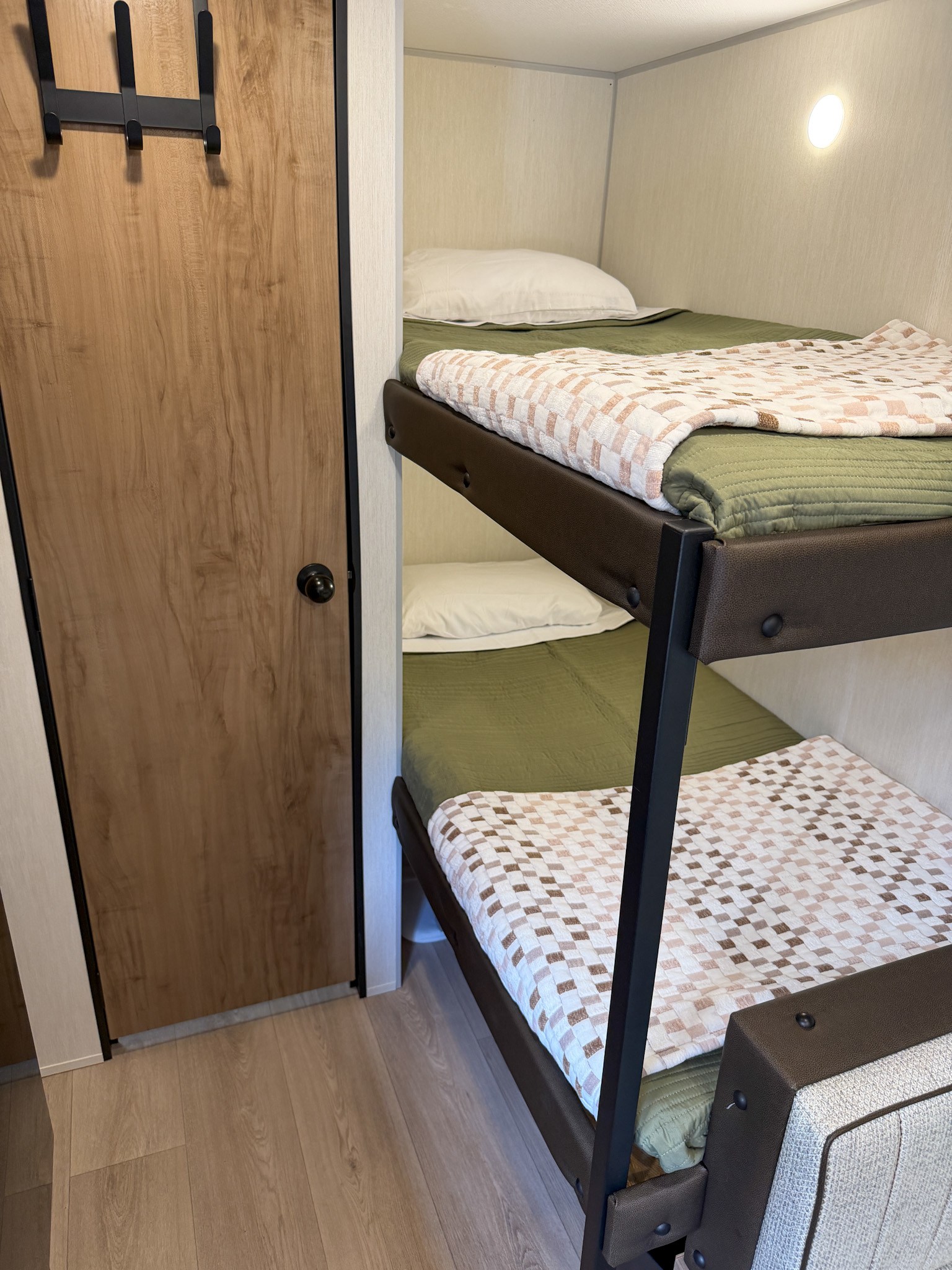 Cozy bunk beds in an RV rental, with green bedding, patterned blankets, a wooden door, and a wall light in a compact space.. Forest River Cherokee Wolf Pup 2025