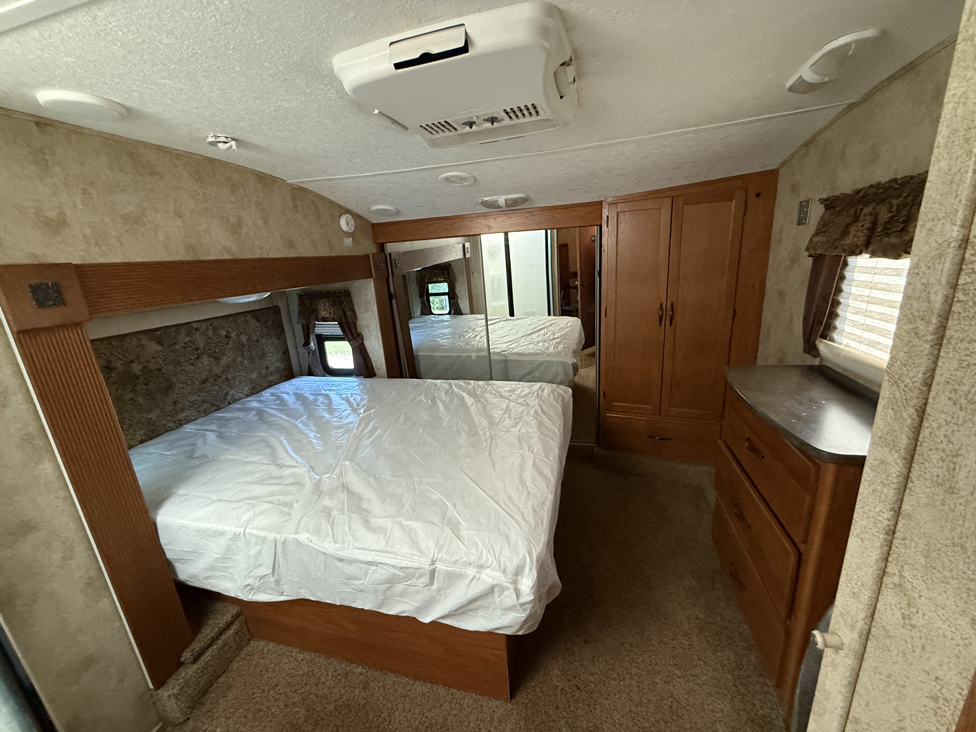 Spacious RV rental bedroom featuring a bed with clean linens, built-in storage, mirrored closet, and AC unit.. Keystone RV Montana Mountaineer 2011