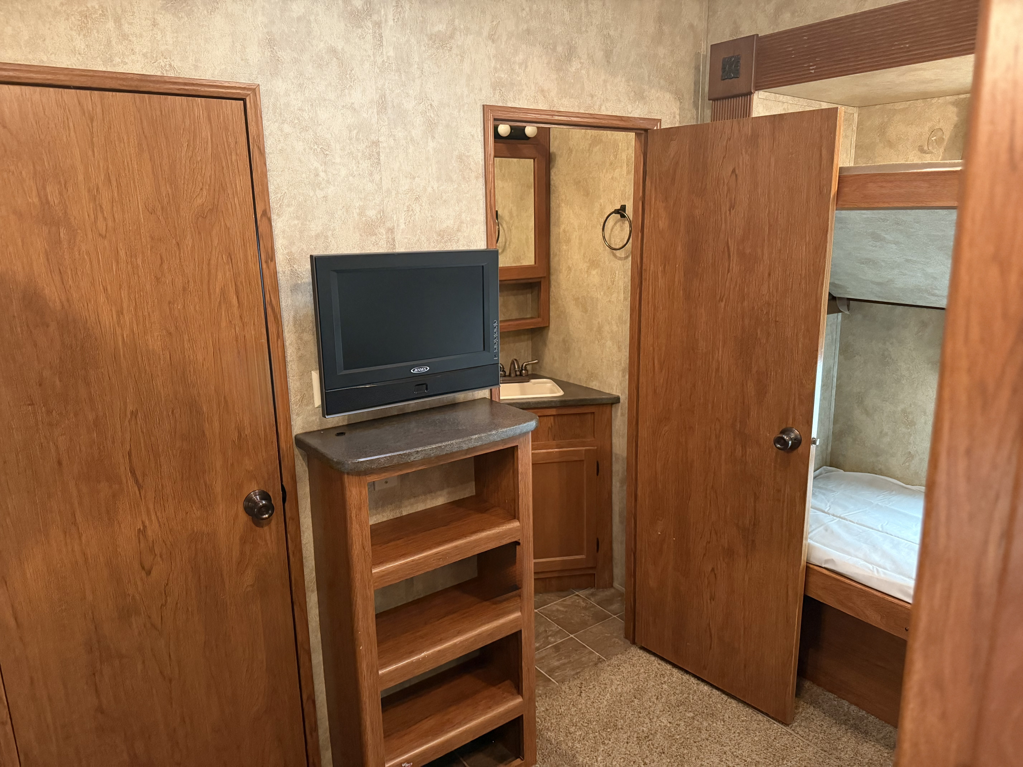 RV rental interior showing a small TV unit, a partial view of a bunk bed, and a compact bathroom with a sink and mirror.. Keystone RV Montana Mountaineer 2011