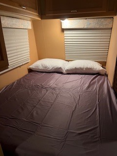 Cozy RV rental bedroom: a comfy bed with pillows, blinds, & overhead storage for your road trip comfort.. Winnebago Warrior 1990