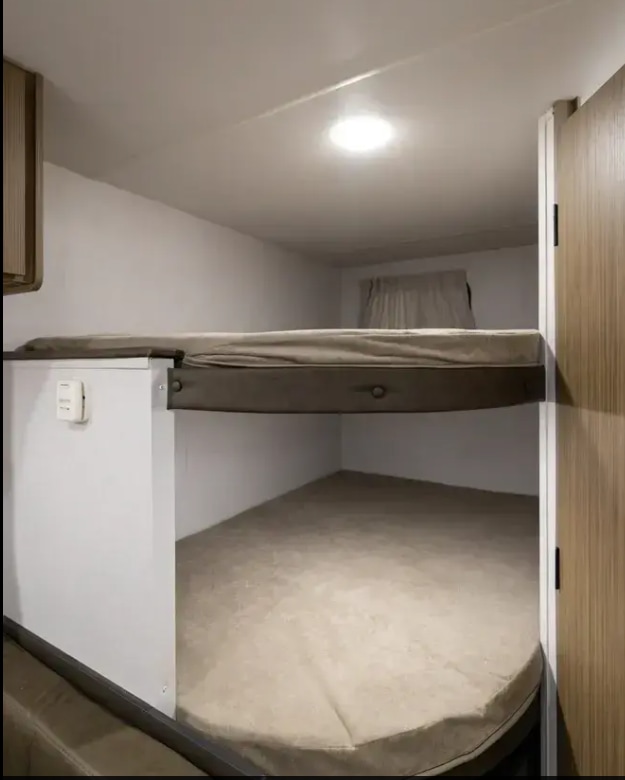 Cozy RV rental bunk beds offer a compact sleeping area with upper/lower mattresses, ceiling light, and thermostat.. Forest River Wildwood FSX 2026