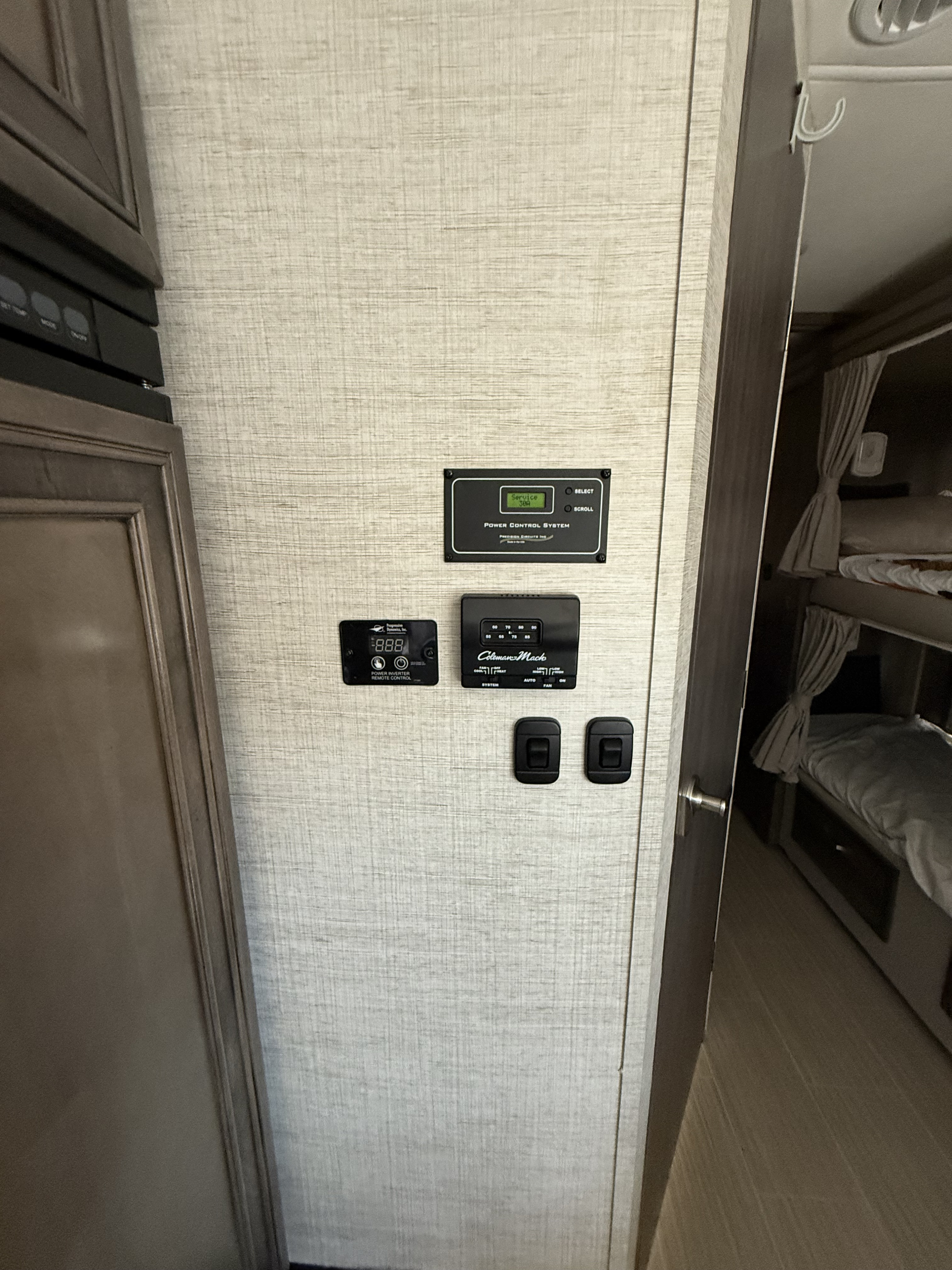 **RV rental** interior showcasing an RV control panel, thermostat, and power inverter display, with bunk beds visible through an open doorway.. Entegra Coach Esteem 2023