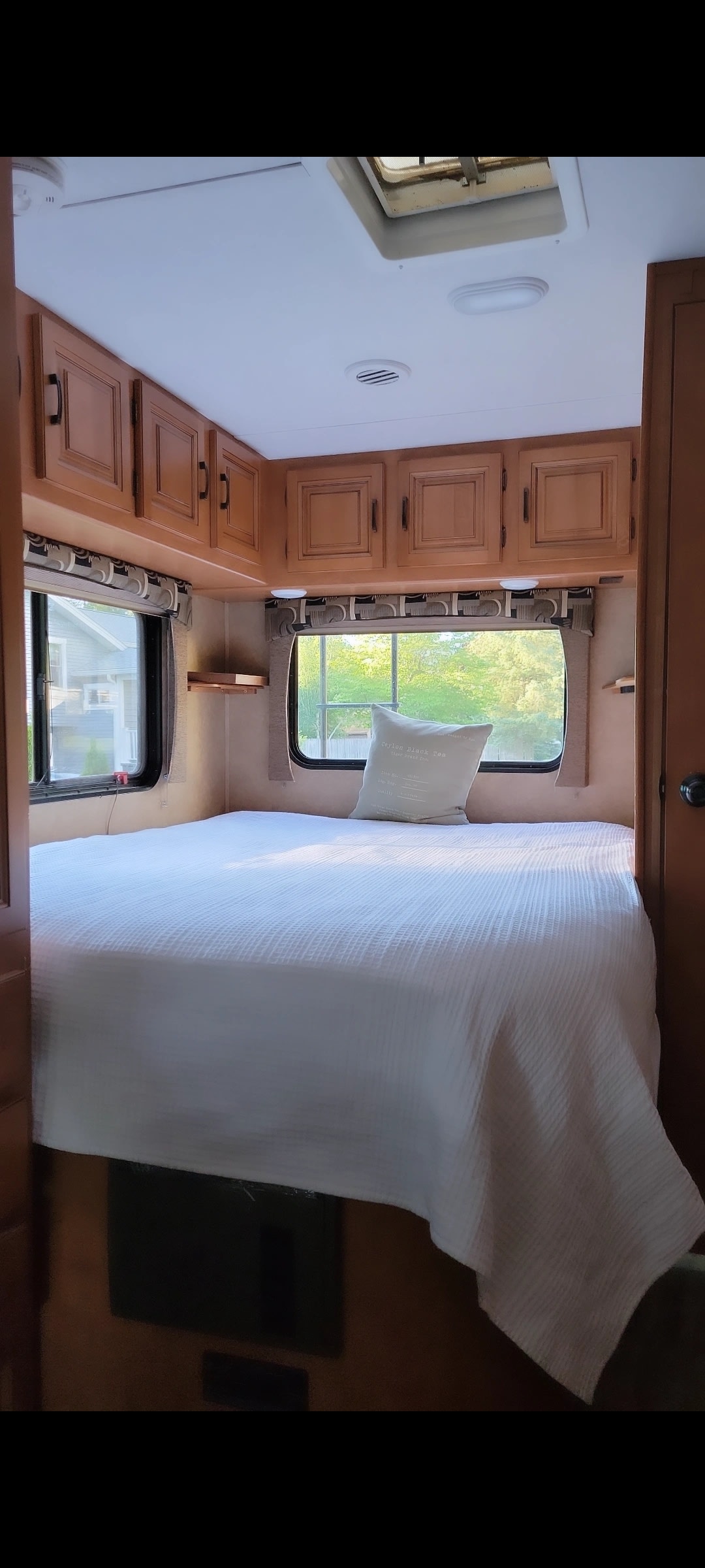 This rv rental offers a cozy bedroom with a white bed, wooden cabinets, and windows with scenic views.. Forest River Sunseeker 2014