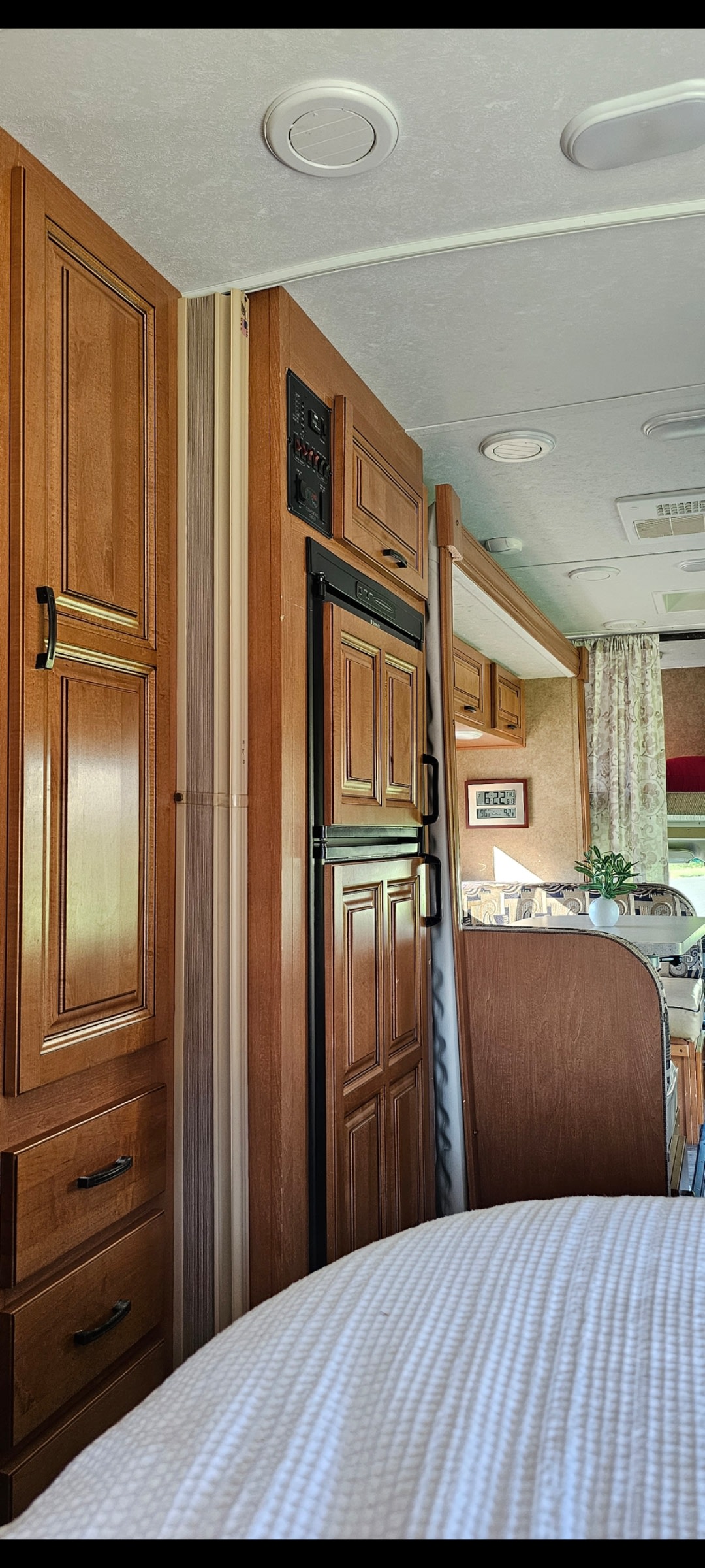 RV rental interior featuring warm wood cabinetry, built-in fridge, and a comfortable bed. Ceiling vents and a dinette are also visible.. Forest River Sunseeker 2014
