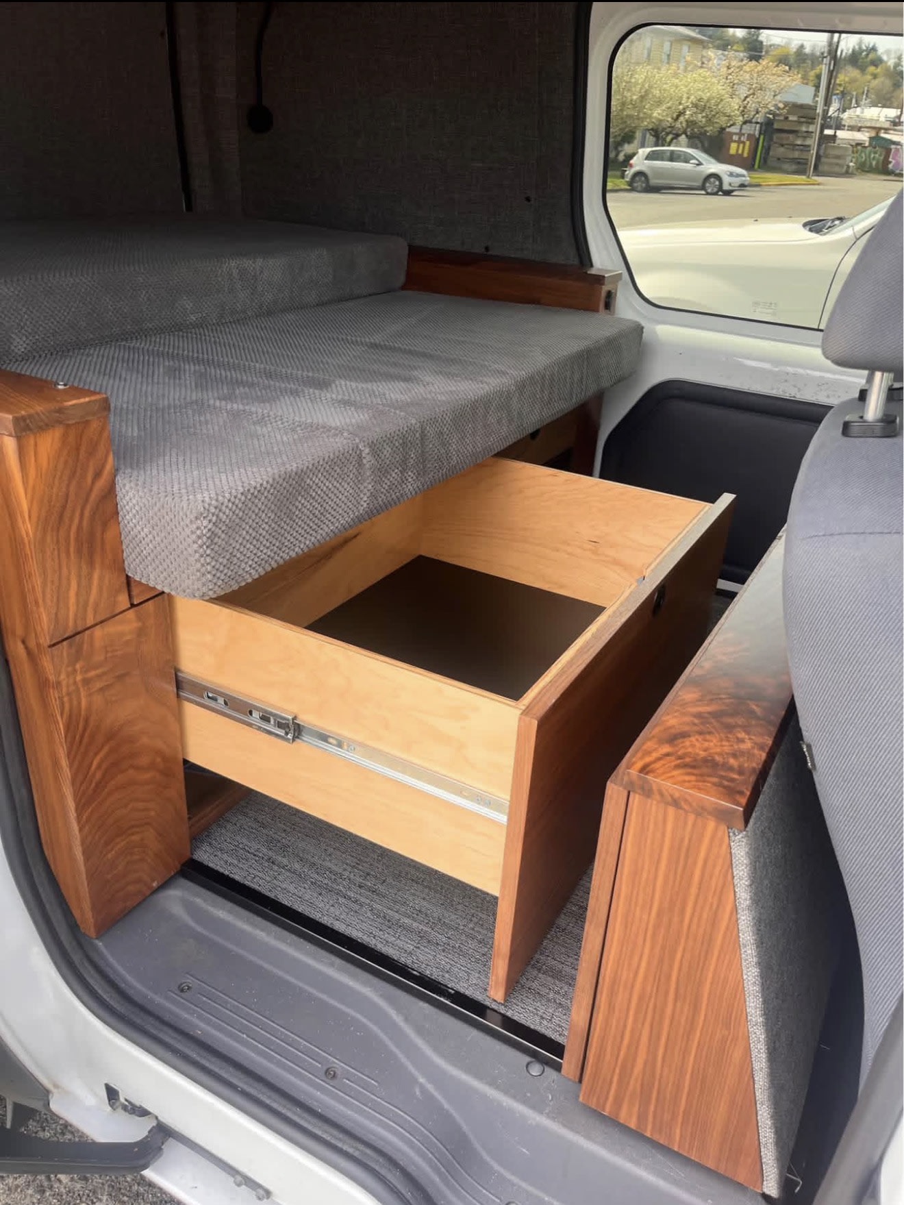 Inside an rv rental: a grey bed, dark wood accents, and a pulled-out storage drawer with light wood interior, visible from the door.. Ford Transit 2013