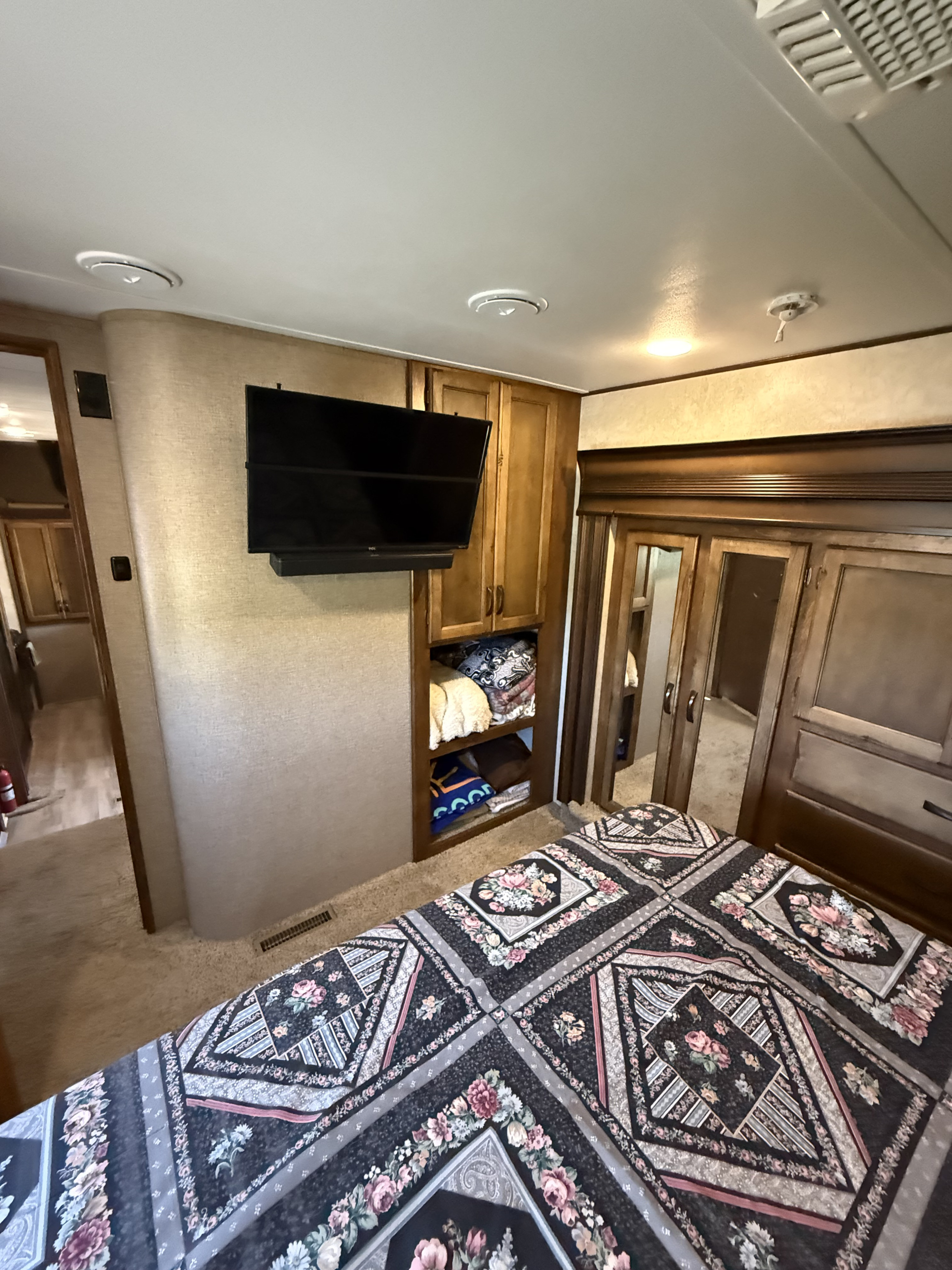 RV rental bedroom with a detailed floral bedspread, wall-mounted TV, and built-in wooden storage cabinets.. Keystone Carbon 2015