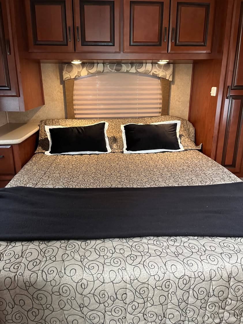 This inviting RV rental bedroom features a patterned bed, black pillows, and rich wood cabinetry, offering cozy comfort.. Lexington Grand Touring 2013