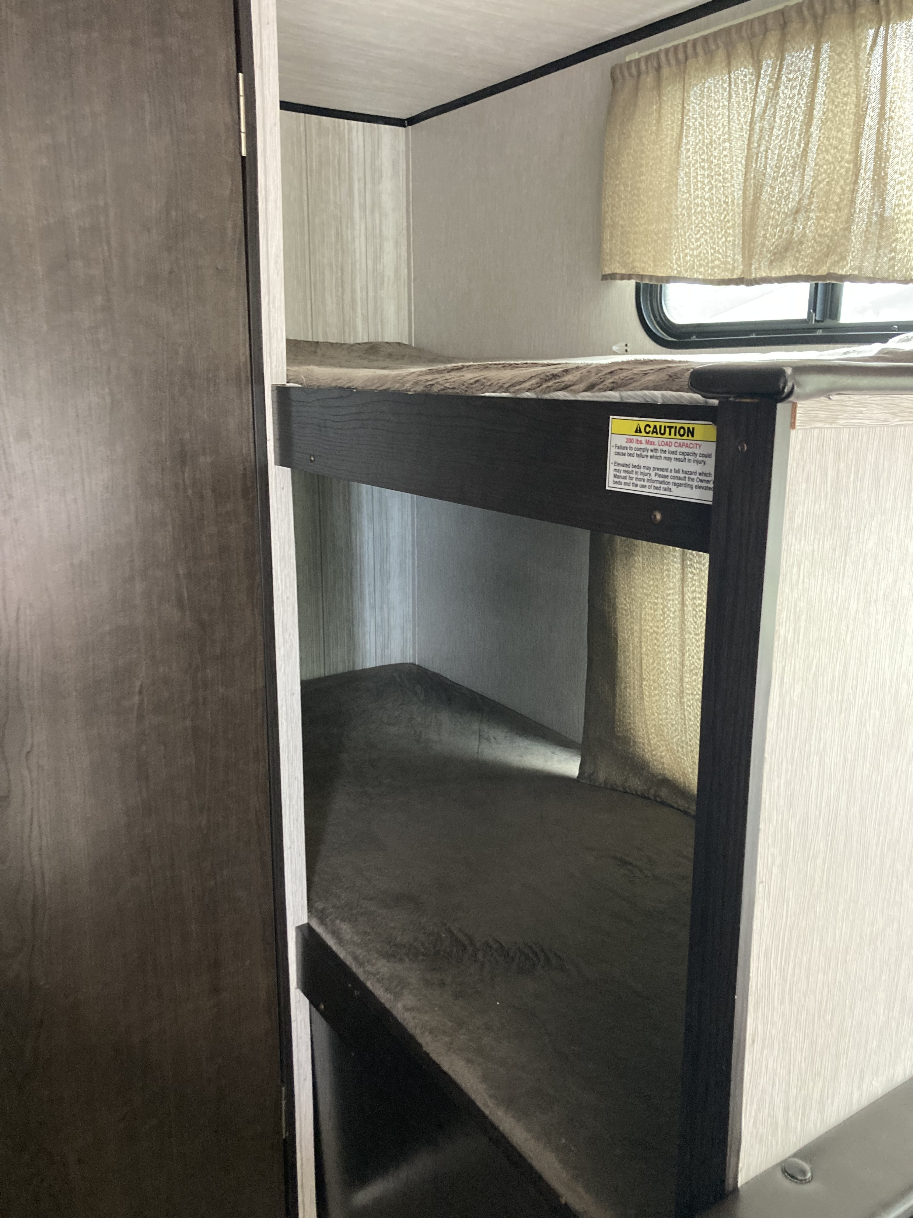 Inside an **rv rental**: cozy bunk beds with a 200 lbs load capacity caution. Ideal sleeping space for travel trailer adventures.. Heartland RVs Pioneer 2019