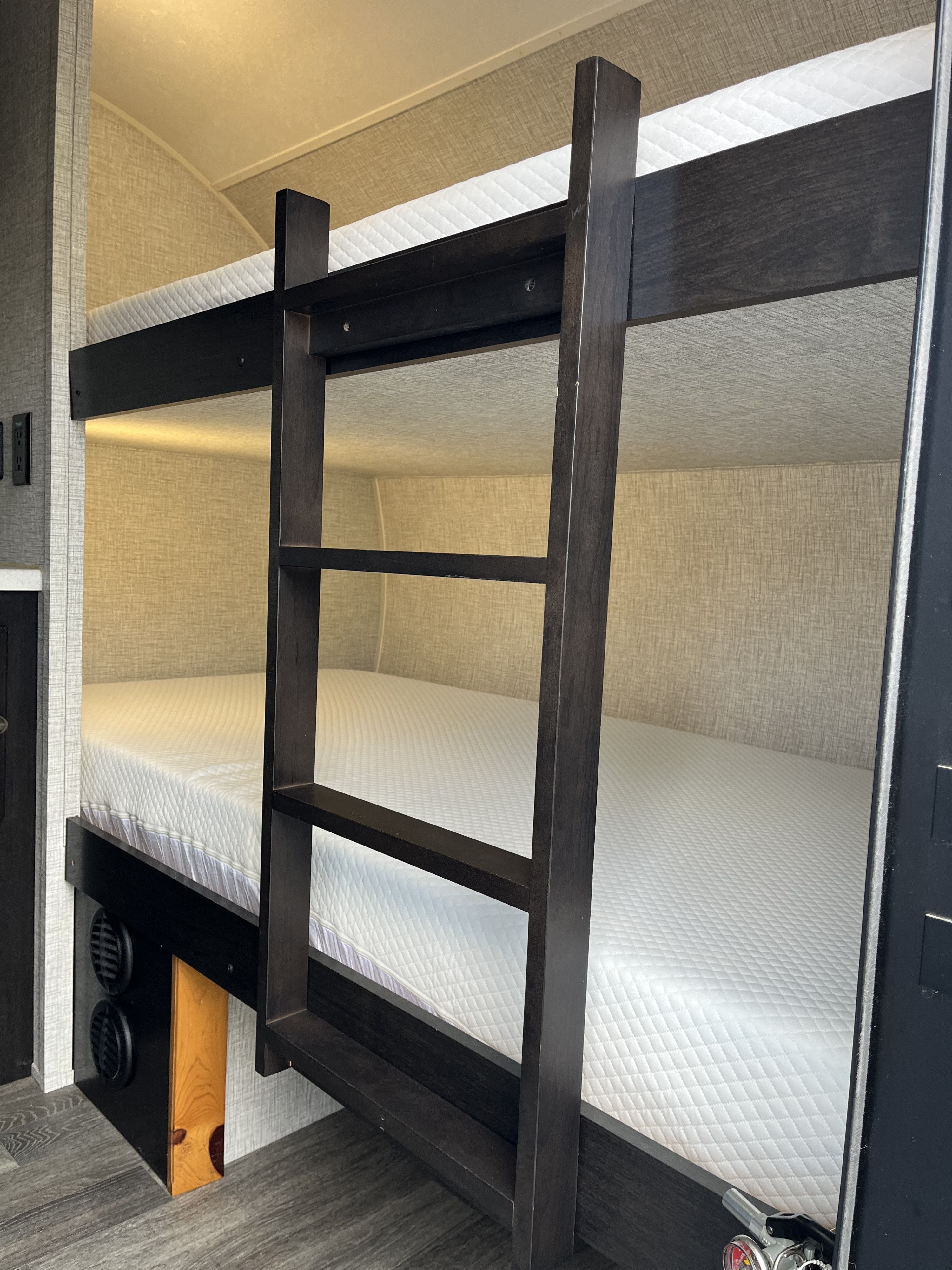 RV rental's modern bunk beds. Dark wood frames, white quilted mattresses, cozy and functional sleeping area.. Braxton Creek Bushwhacker Plus 2024