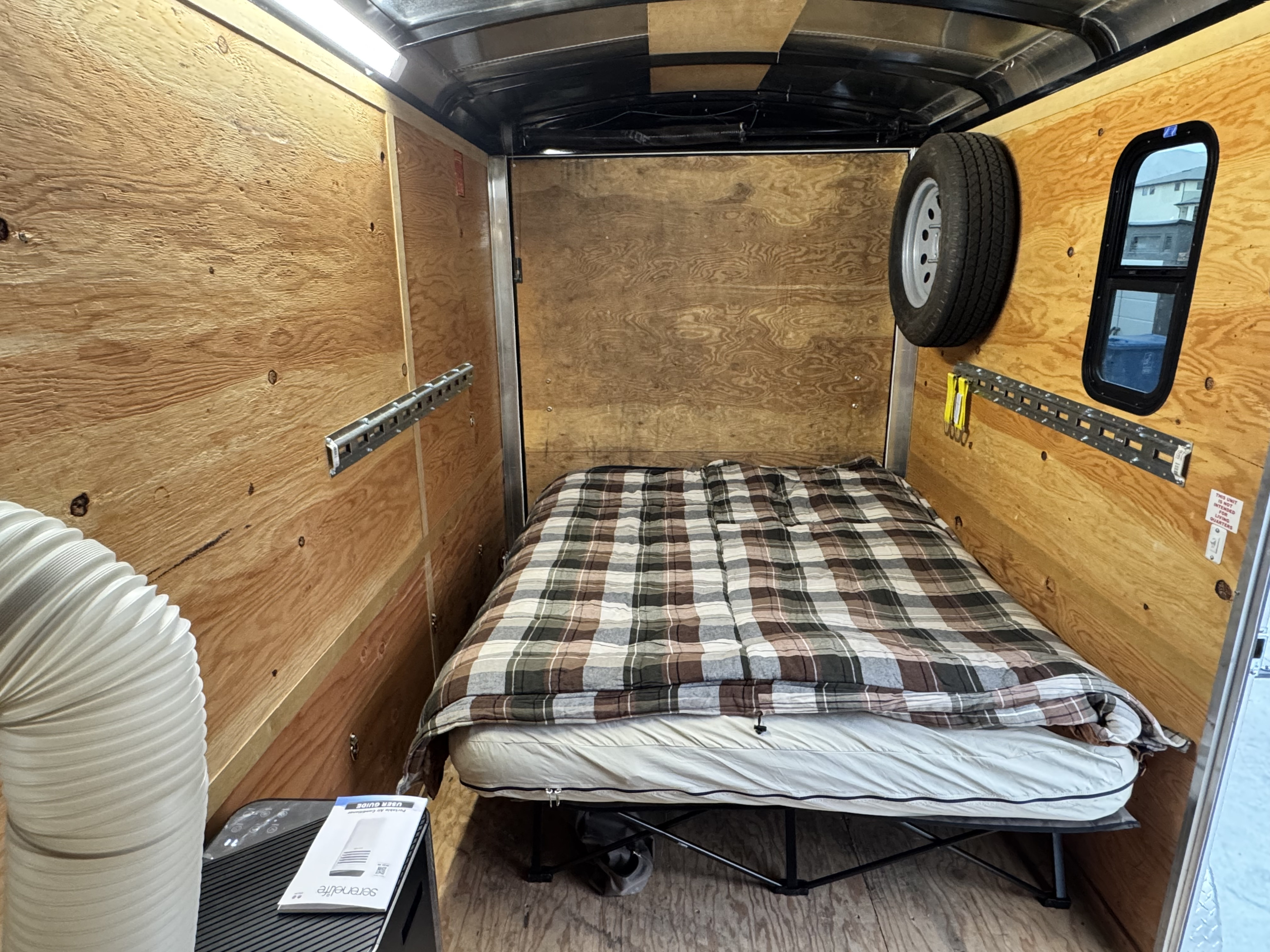 Inside a minimalist camper conversion: A cozy bed, portable AC, and spare tire on wood-paneled walls, ideal for an rv rental.. Mirage MXL612SA 2015